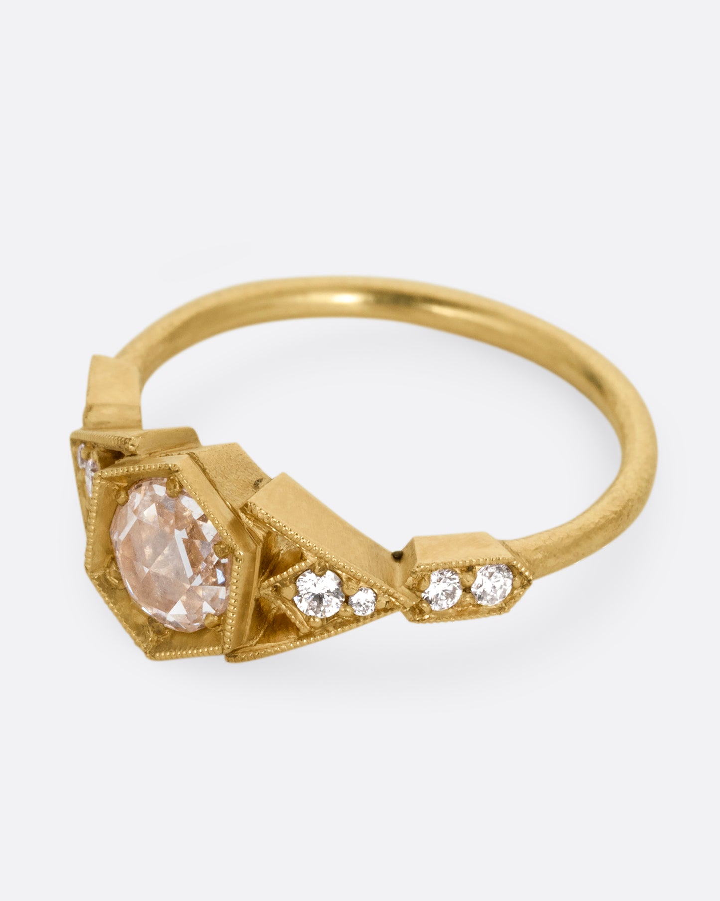 A yellow gold ring with a center diamond and angular side cutouts and diamond accents. Shown from the side.