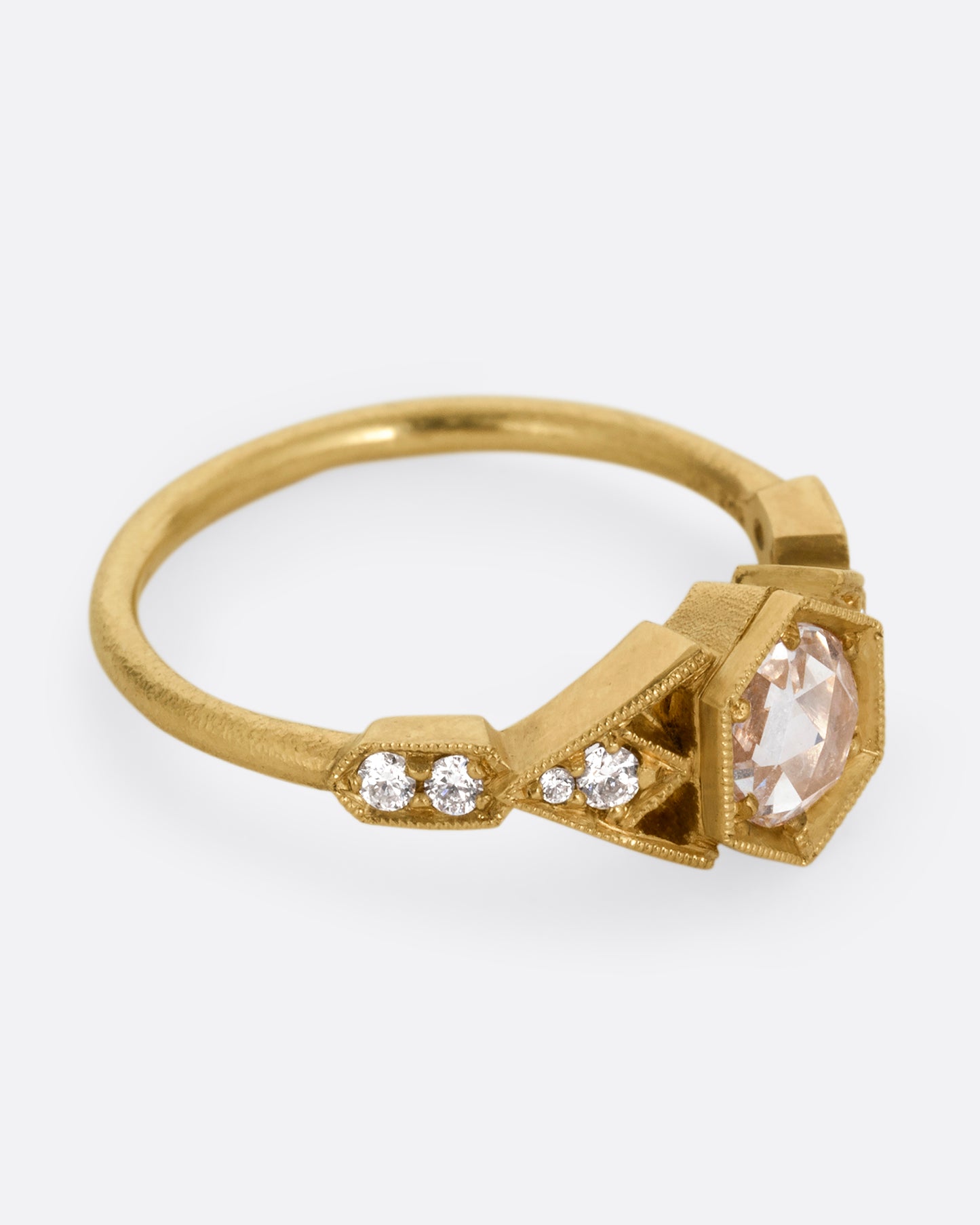 A yellow gold ring with a center diamond and angular side cutouts and diamond accents. Shown from the side.