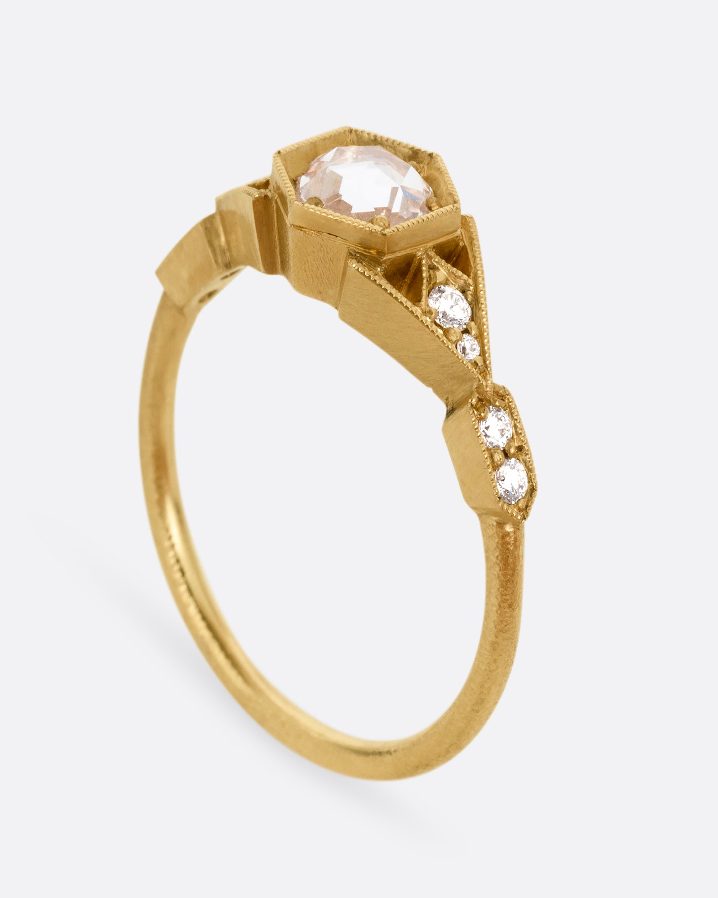 A yellow gold ring with a center diamond and angular side cutouts and diamond accents. Shown standing up from the side.