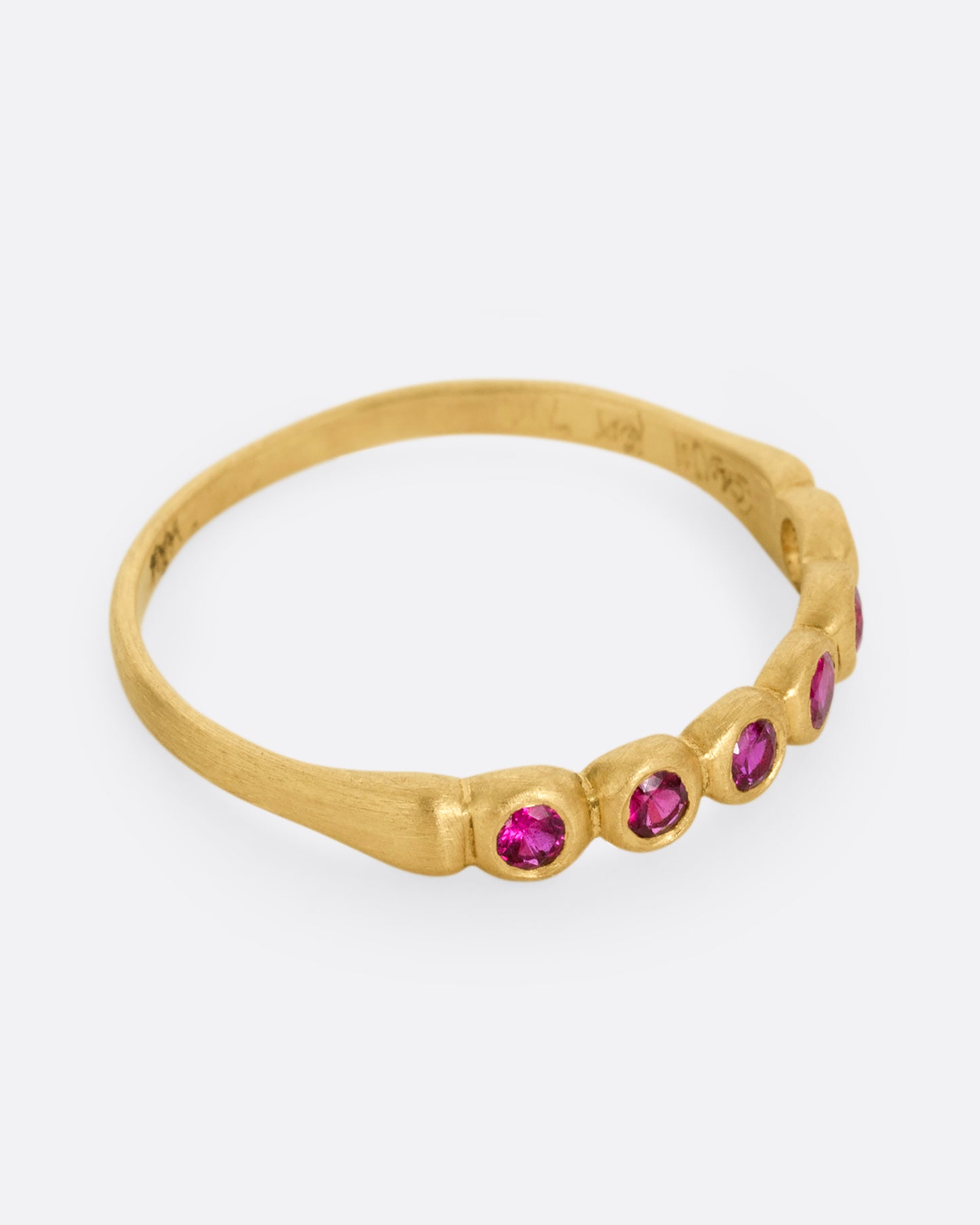 A yellow gold ring with six bezel set rubies. Shown from the side.