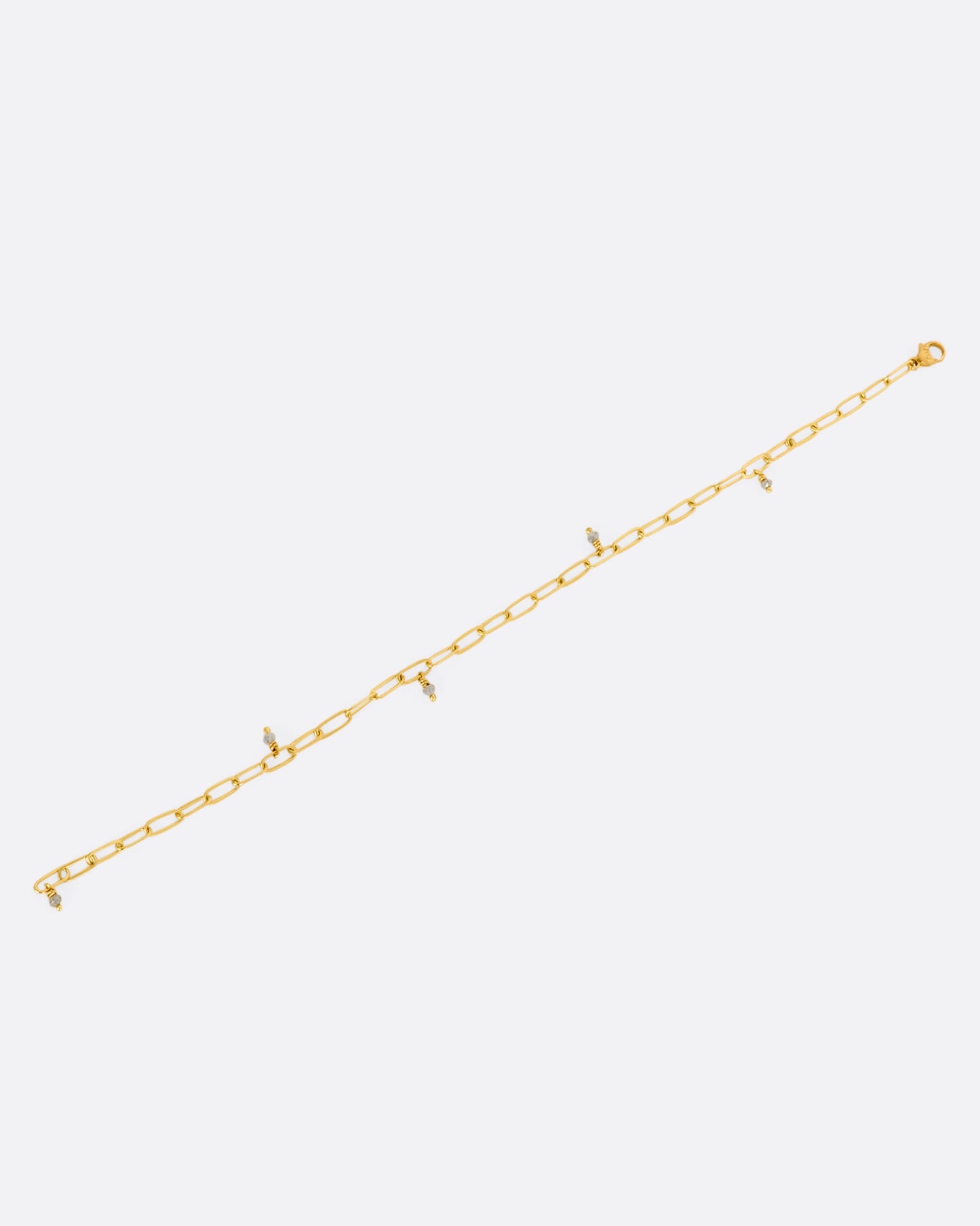 A yellow gold oval link bracelet with 5 tiny raw diamond beads spaced throughout. View lying flat, from above, not closed.