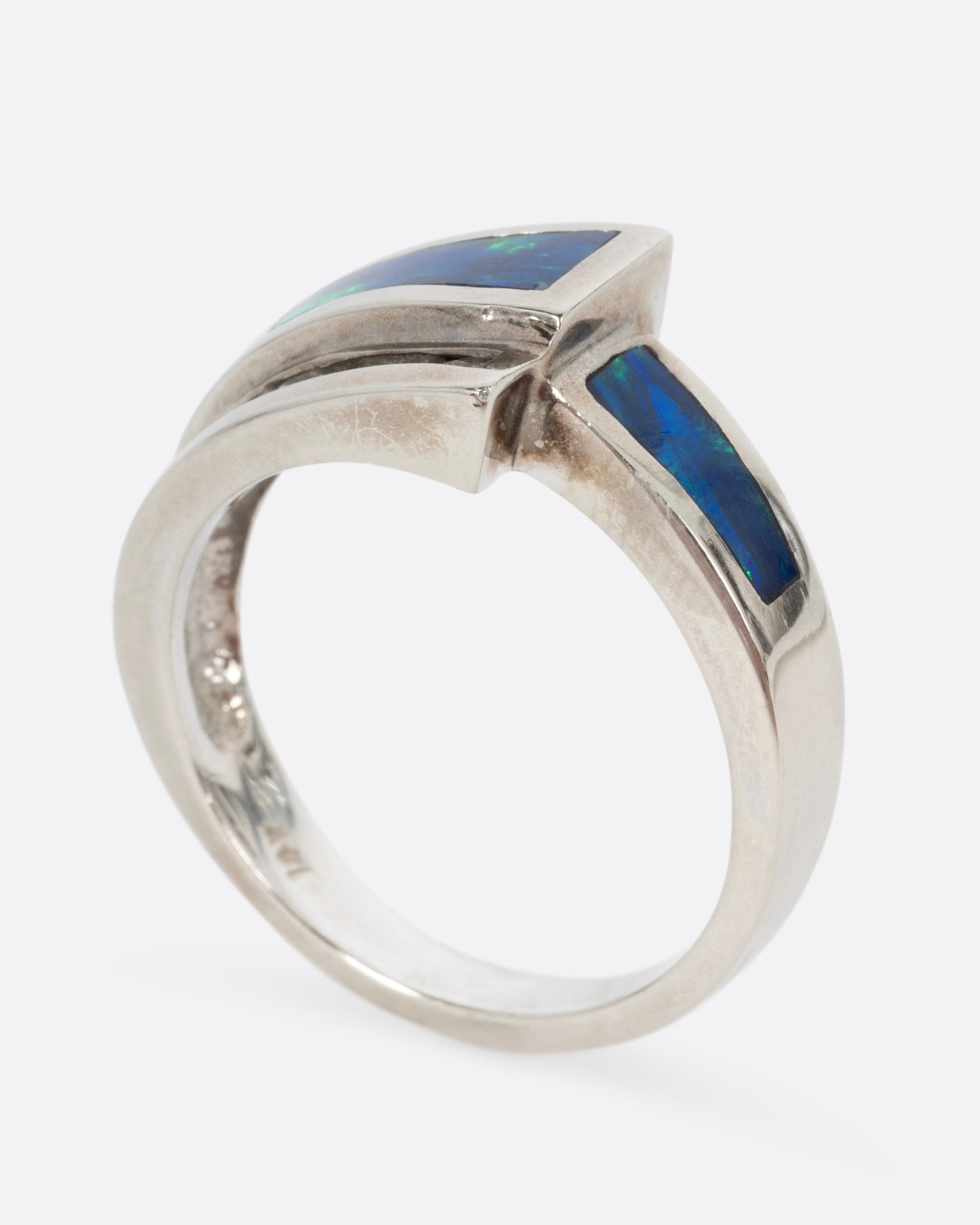 A white gold wrap ring with opal inlay and a queue of diamonds along the edge, shown standing up from the side.