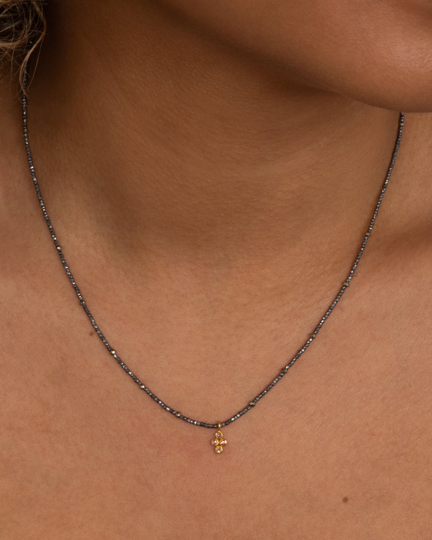 A pyrite bead necklace with a diamond quartet charm at the center. Shown from the front on a person.
