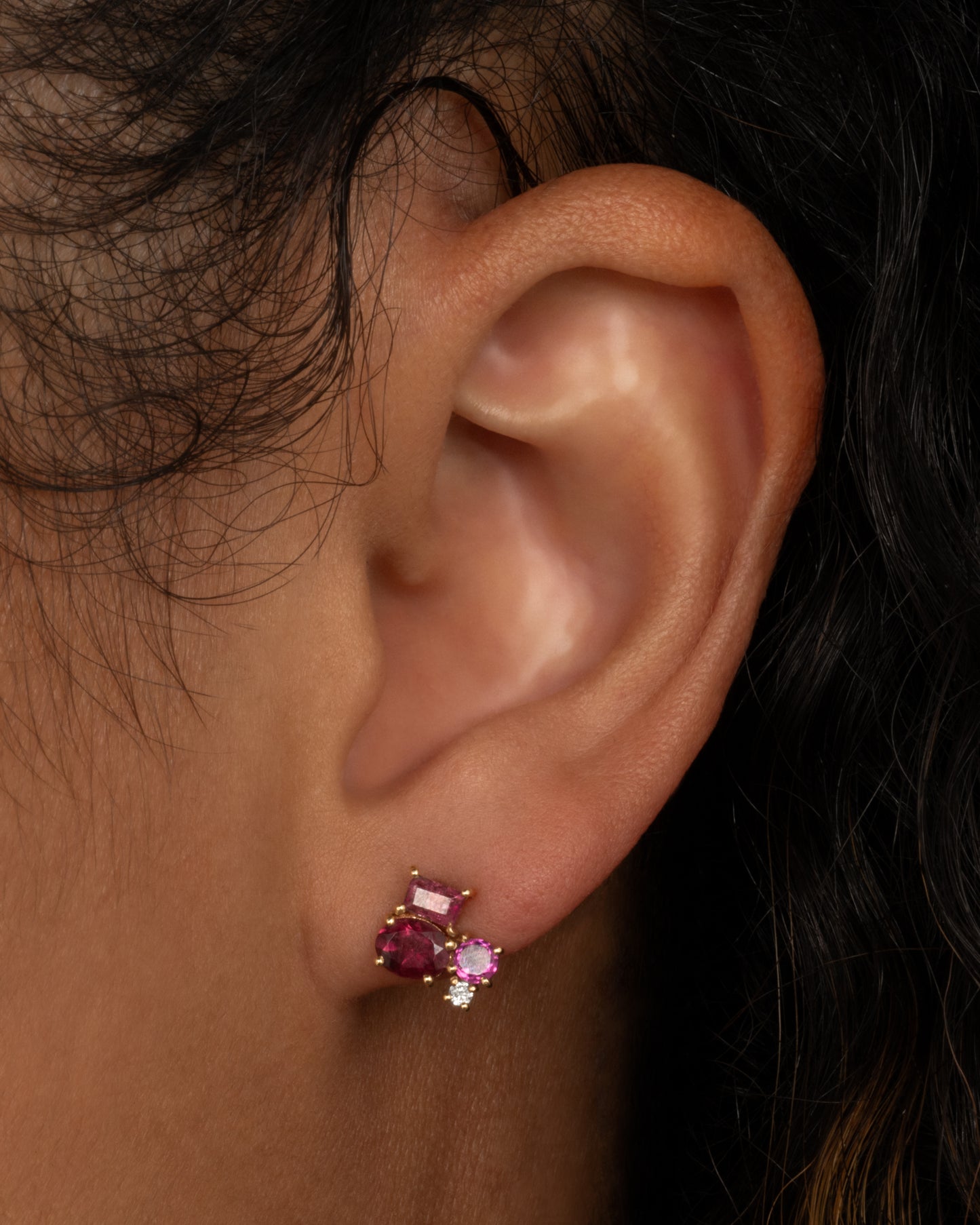 A yellow gold stud earring with a mosaic of prong set tourmalines. Shown worn in an ear.