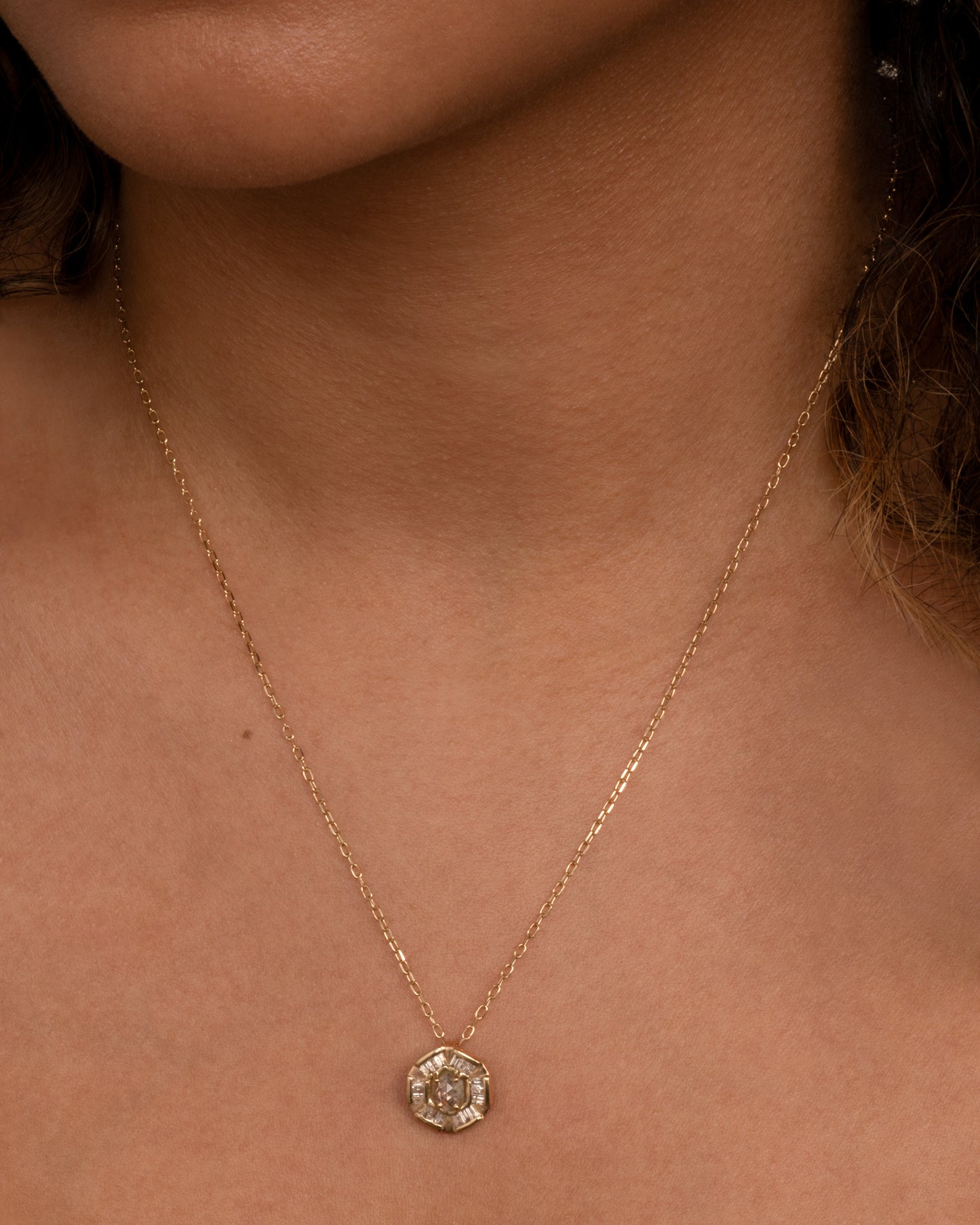 An alternative to a classic medal, this round pendant has a rose cut diamond at its center and is lined with baguettes. Shown worn around the neck.
