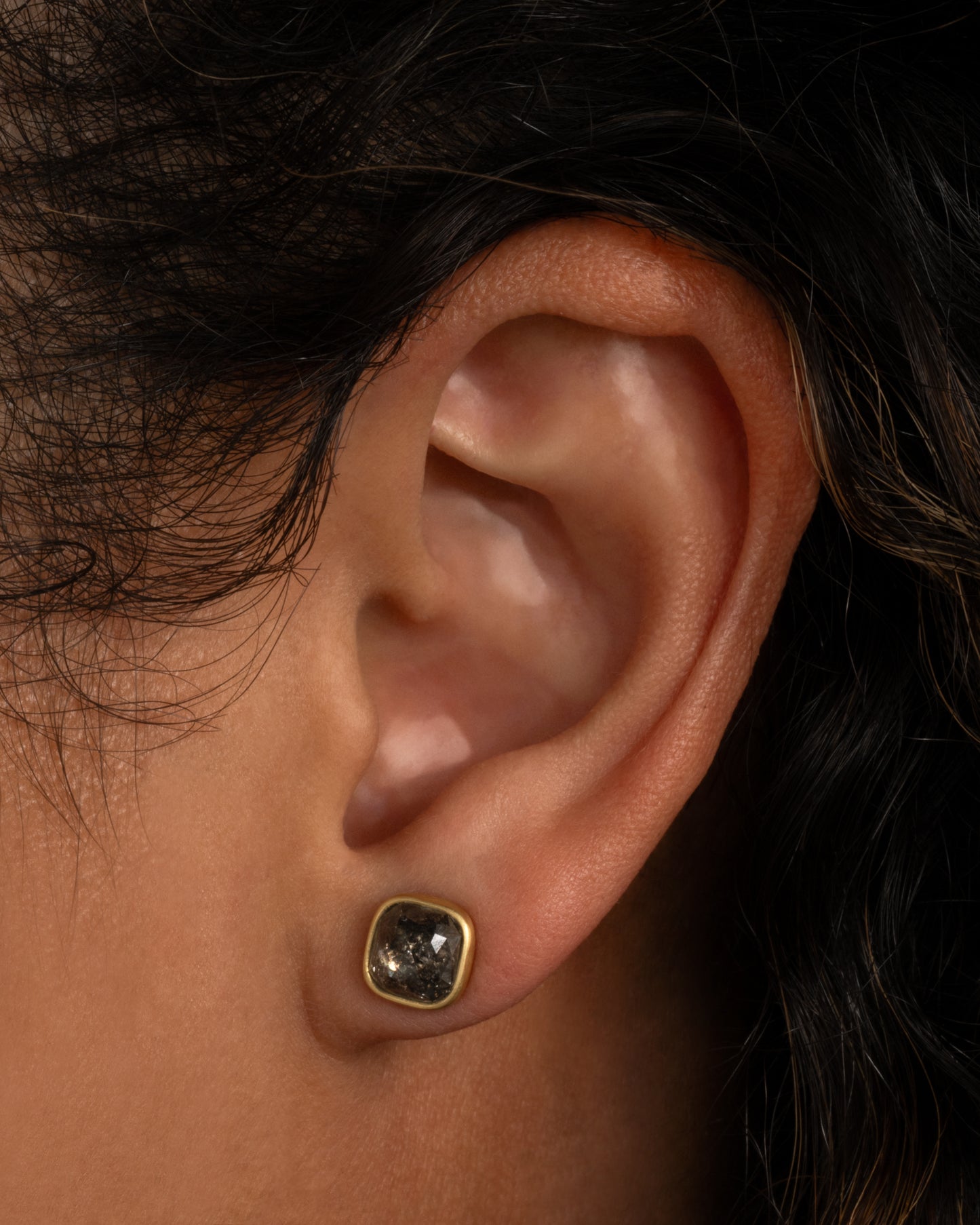 A yellow gold square salt and pepper stud earring, shown from the front on an ear.