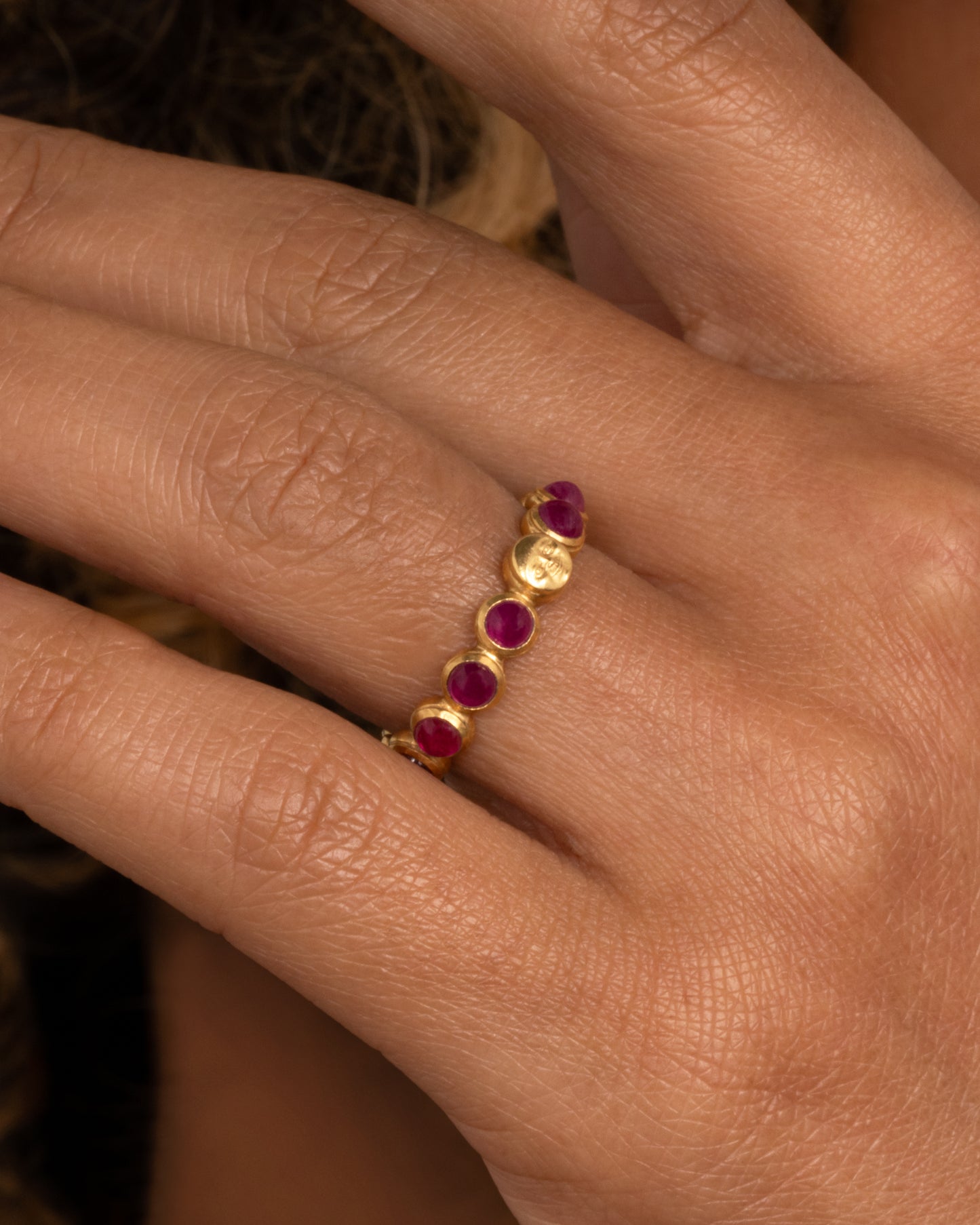 A yellow gold eternity band with ruby cabochons and one moonface. Shown from the side worn on finger.