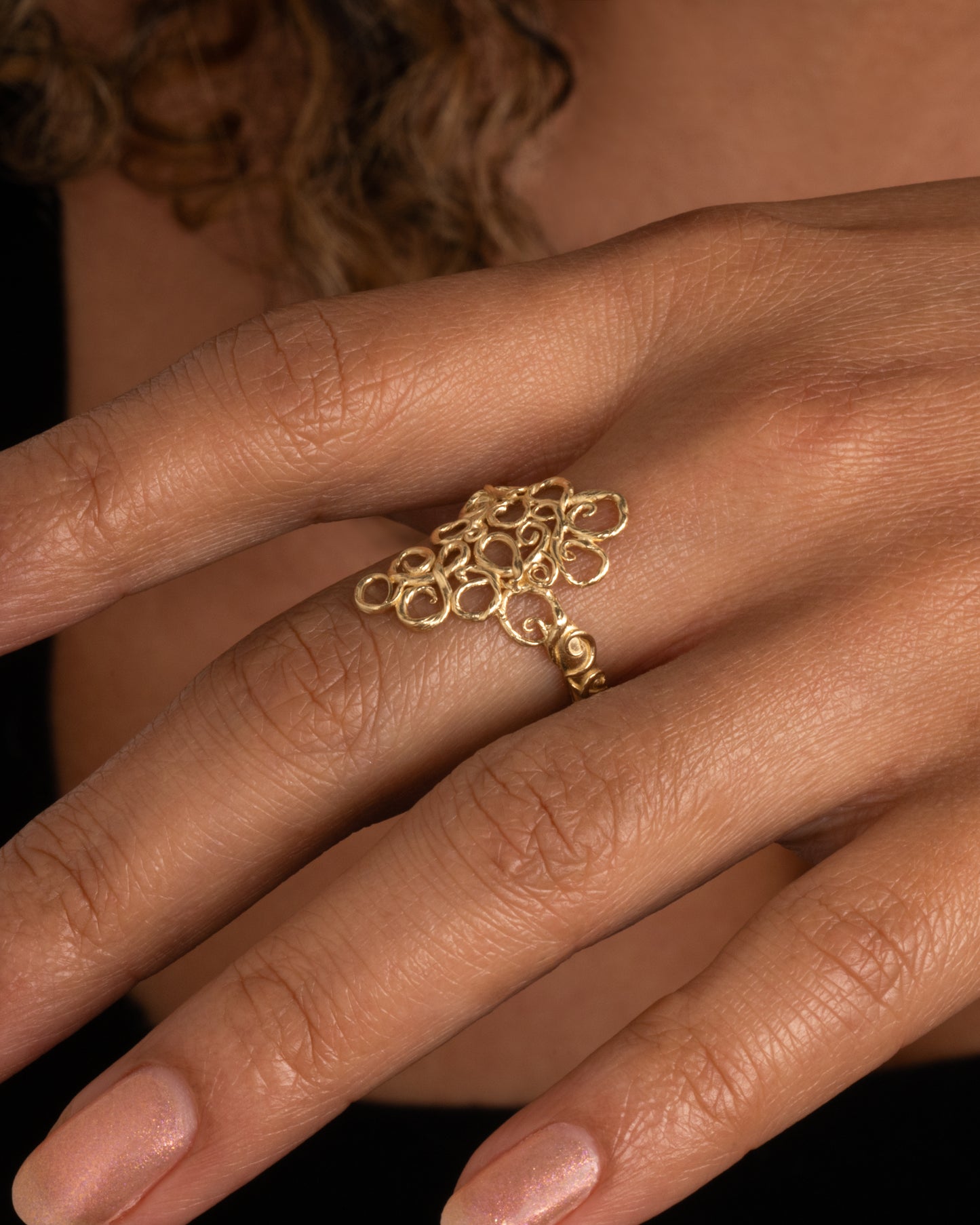 A yellow gold ring with filigree in the shape of a diamond at its center. Shown worn on hand.