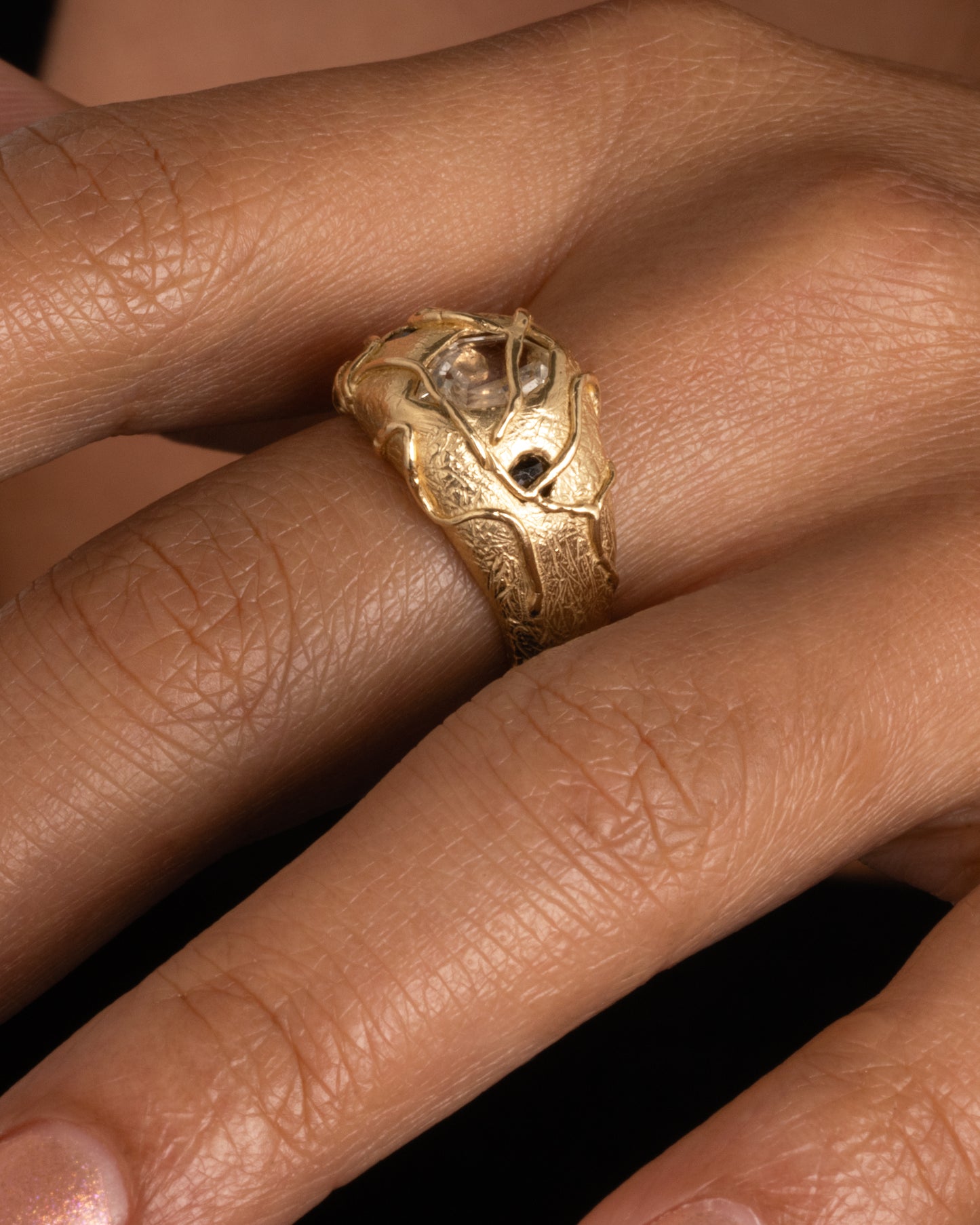 A chunky yellow gold ring with a vine motif that looks like it's grown over the fancy step cut sapphire at the center and the brilliant black diamonds. Shown worn on hand.