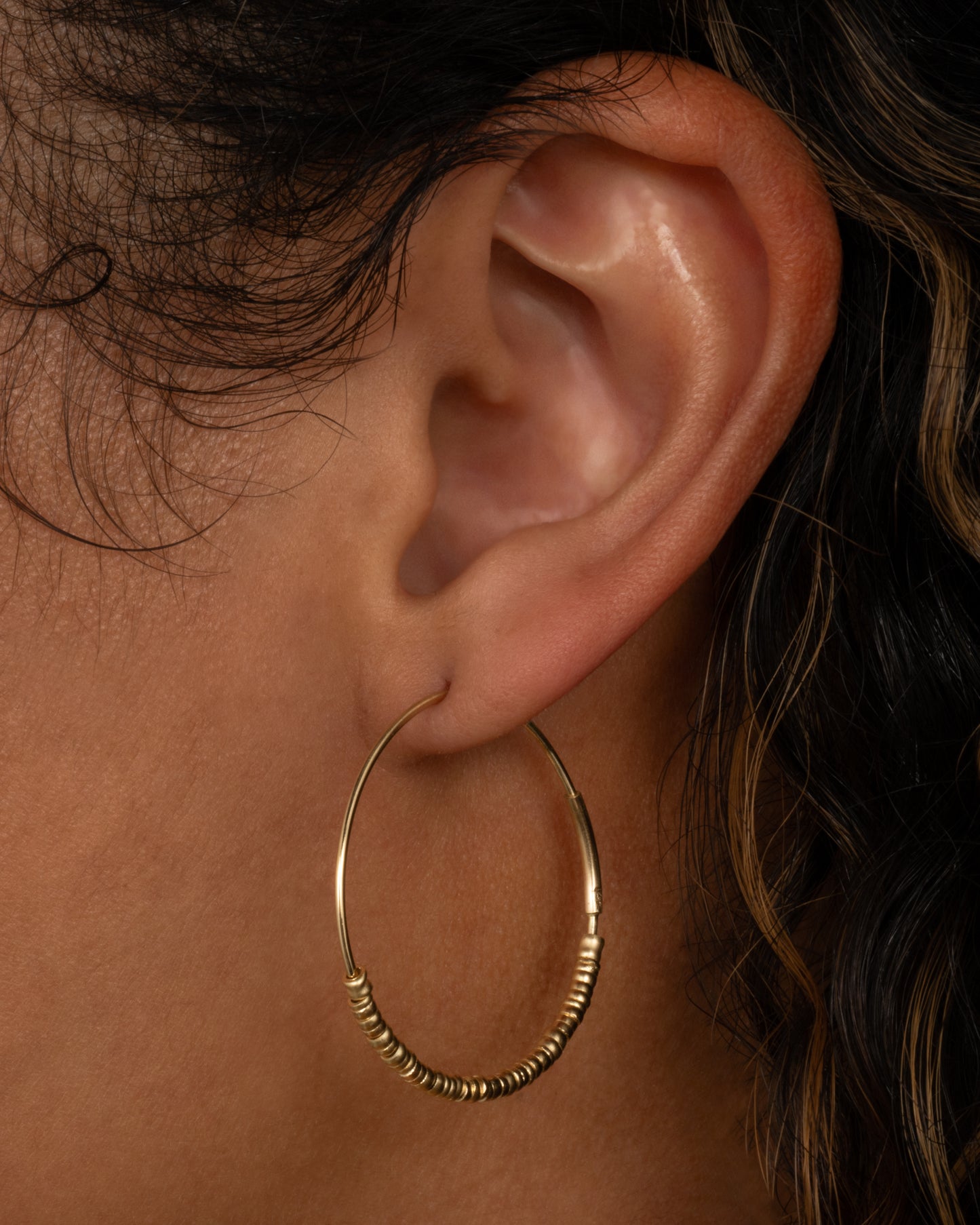 A yellow gold hoop earring with freely moving beads. Shown on a person from the side.