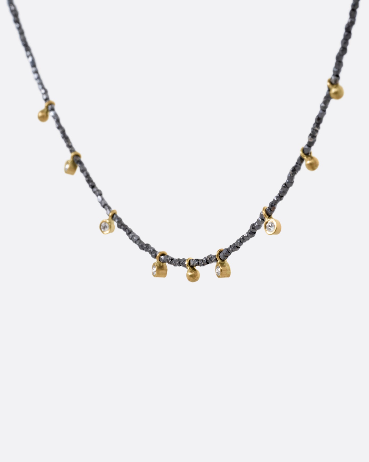 A necklace with five bezel set diamond charms and four gold drops interspersed among oxidized silver beads. Shown from the side.