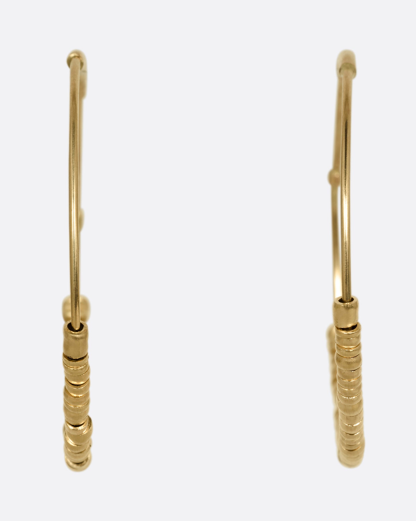 A pair of yellow gold hoop earrings with freely moving beads. Shown from the front.