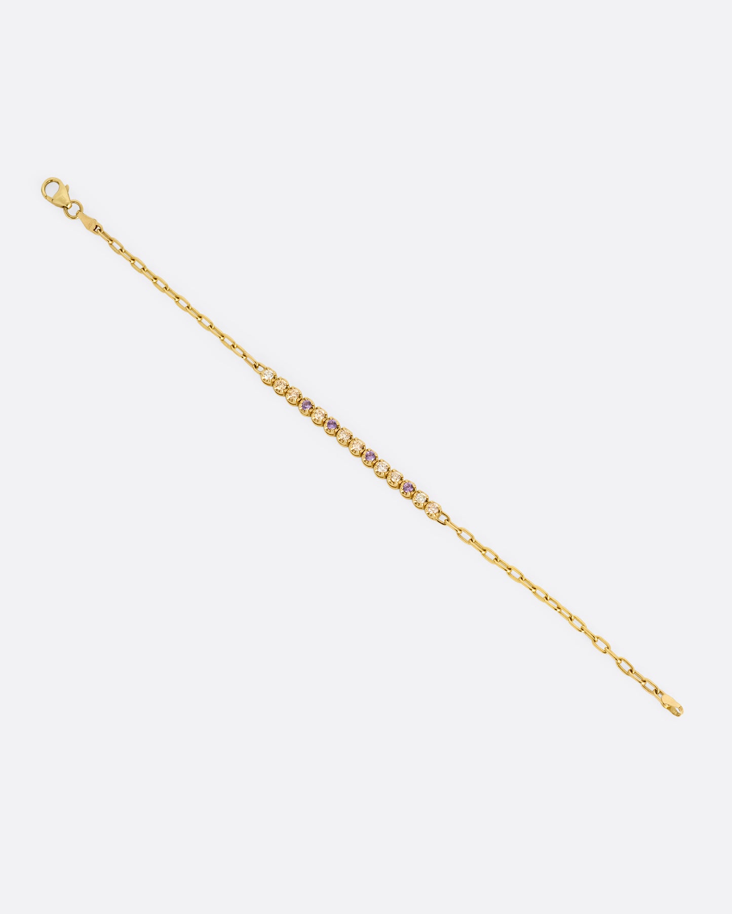 A yellow gold partial tennis bracelet with peach and yellow diamonds and purple sapphires. Shown from the front.