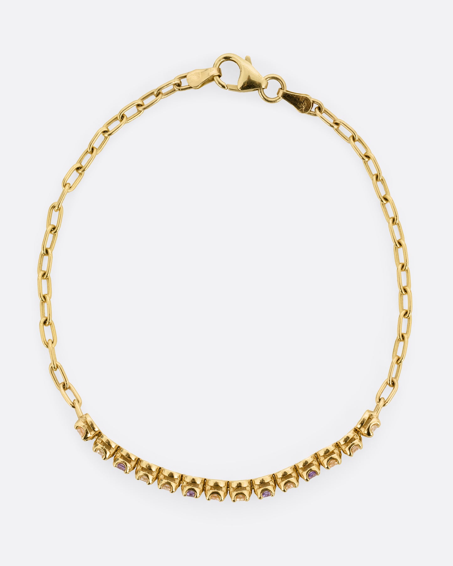 A yellow gold partial tennis bracelet with peach and yellow diamonds and purple sapphires. Shown from the top.