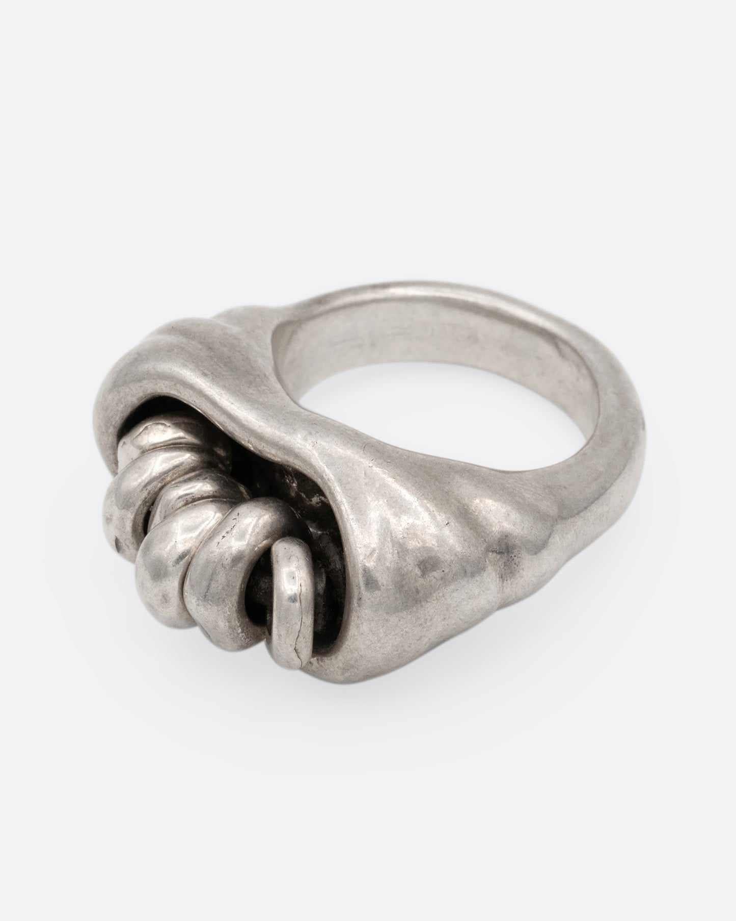 A silver ring with a cluster of free moving hoops nestled into its towering face. Shown from the side.