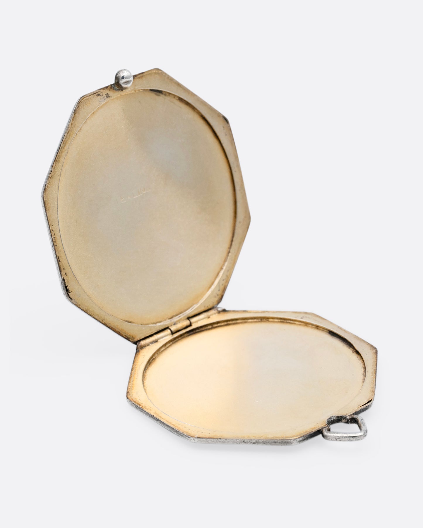 An octagonal silver locket with intricate stripe engravings and a scrolling letter 'C'. Shown open lying flat.