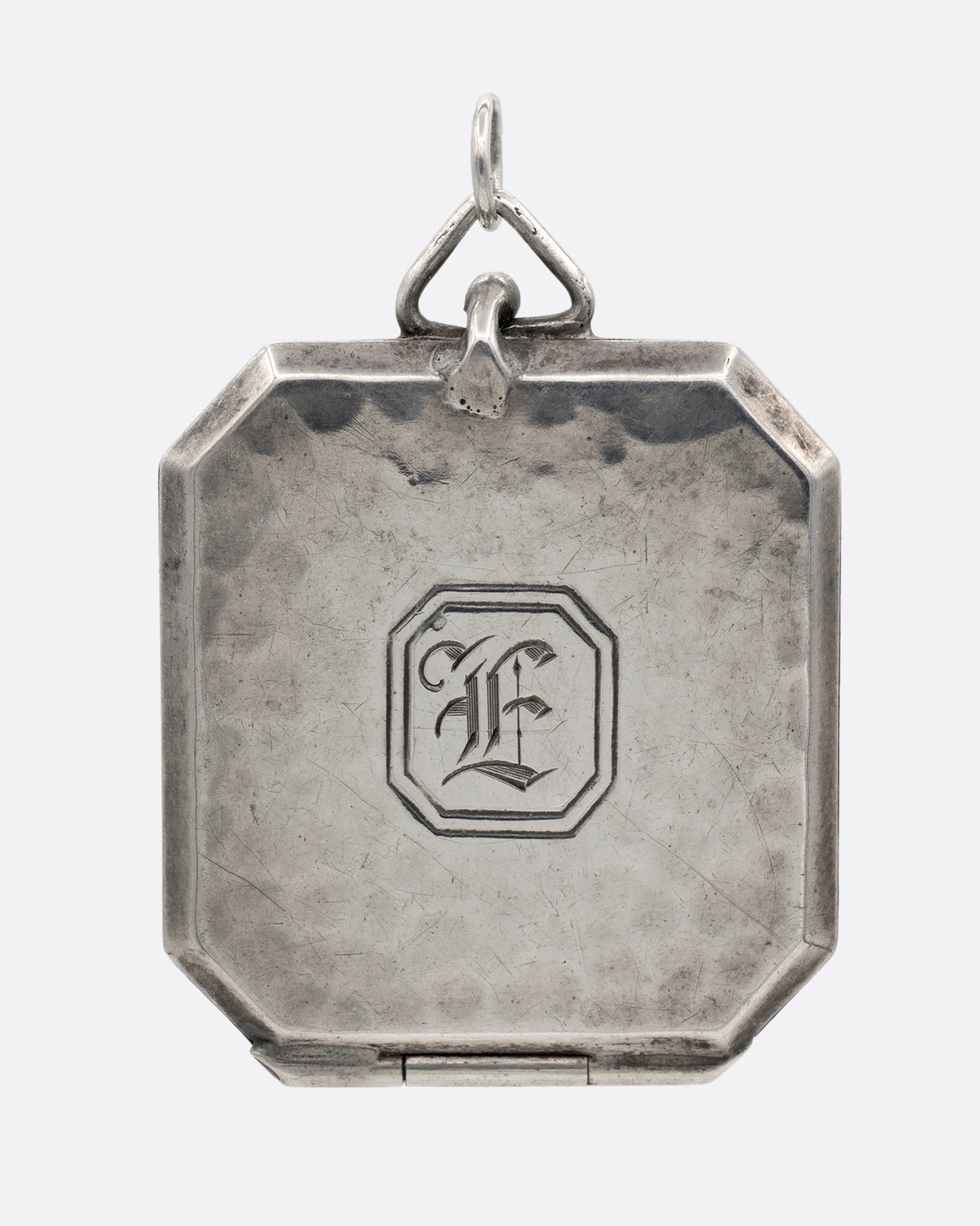 A silver octagonal locket with an 'E' engraved a its center. Shown from the front.