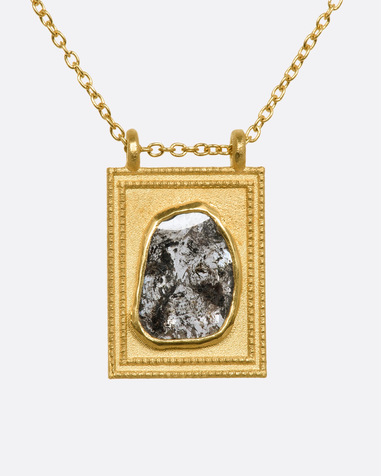 A yellow gold rectangular pendant with a textured border featuring a rose cut salt and pepper diamond hanging from a cable chain. View from the front.