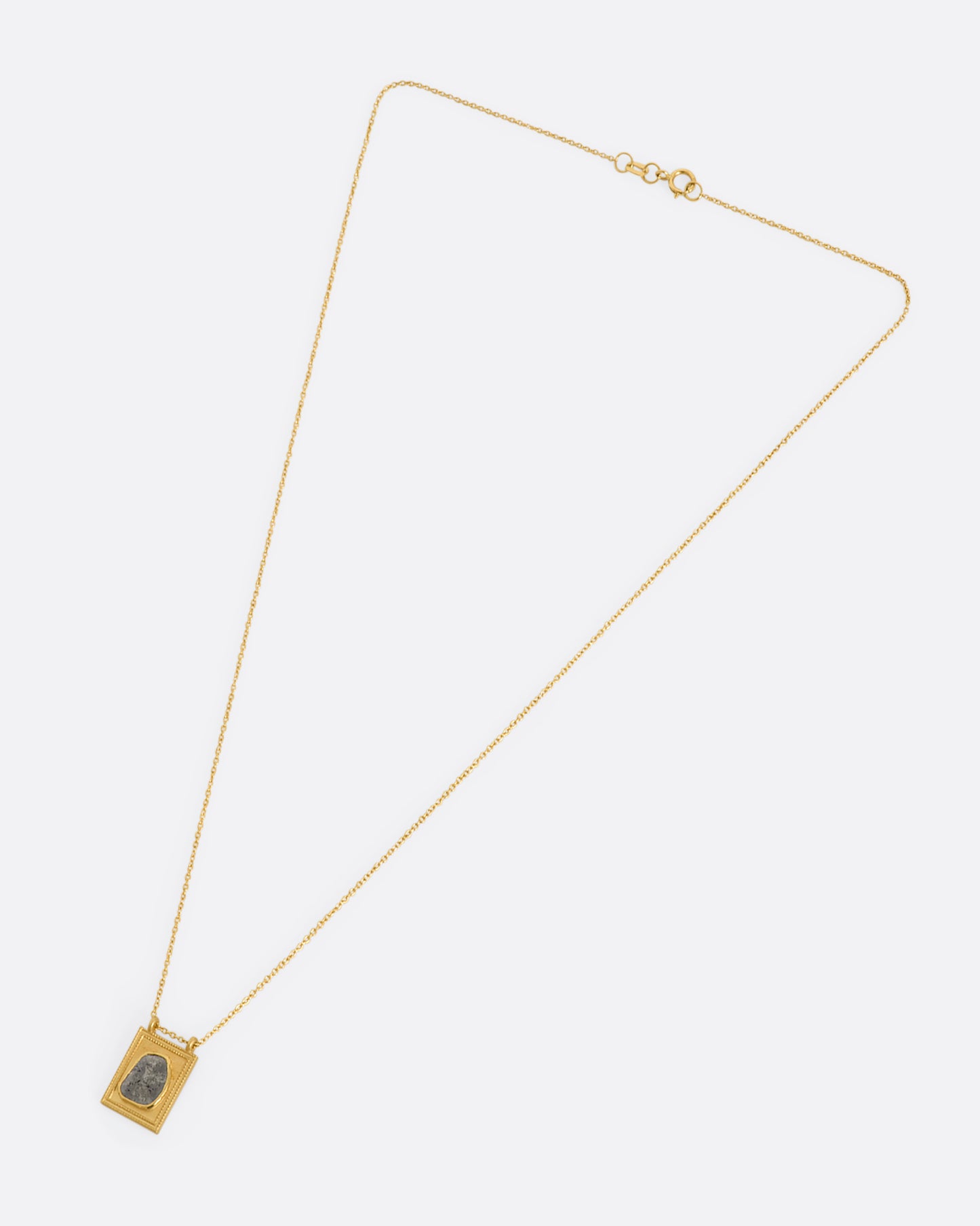 A yellow gold rectangular pendant with a textured border featuring a rose cut salt and pepper diamond hanging from a cable chain. View of the entire necklace laying flat.