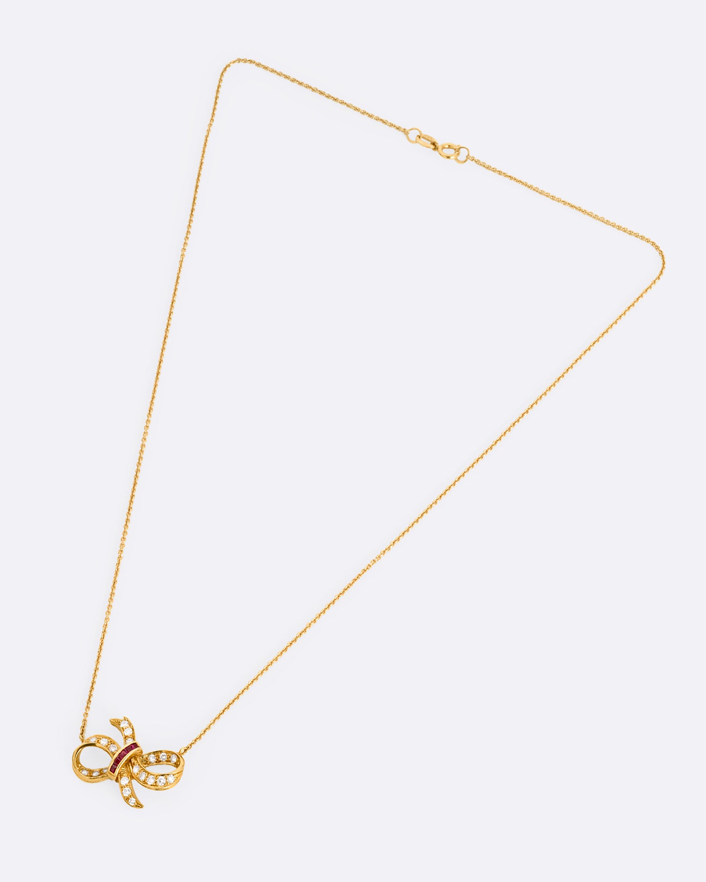 A yellow gold cable chain necklace with a diamond and ruby studded bow at the center. Shown from the front.