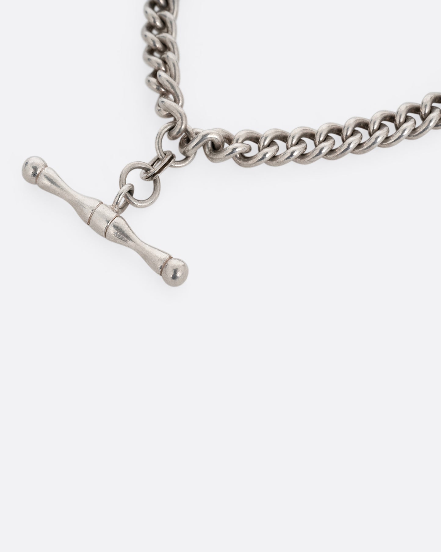 A close up of a silver curb chain pocket watch curb chain necklace with a T-bar on one end.