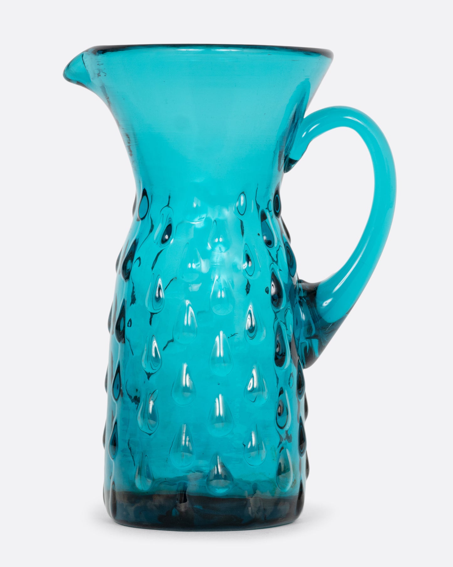 A teal glass creamer with a funnel shaped top, handle, and a bubbly teardrop pattern. Shown from the side.