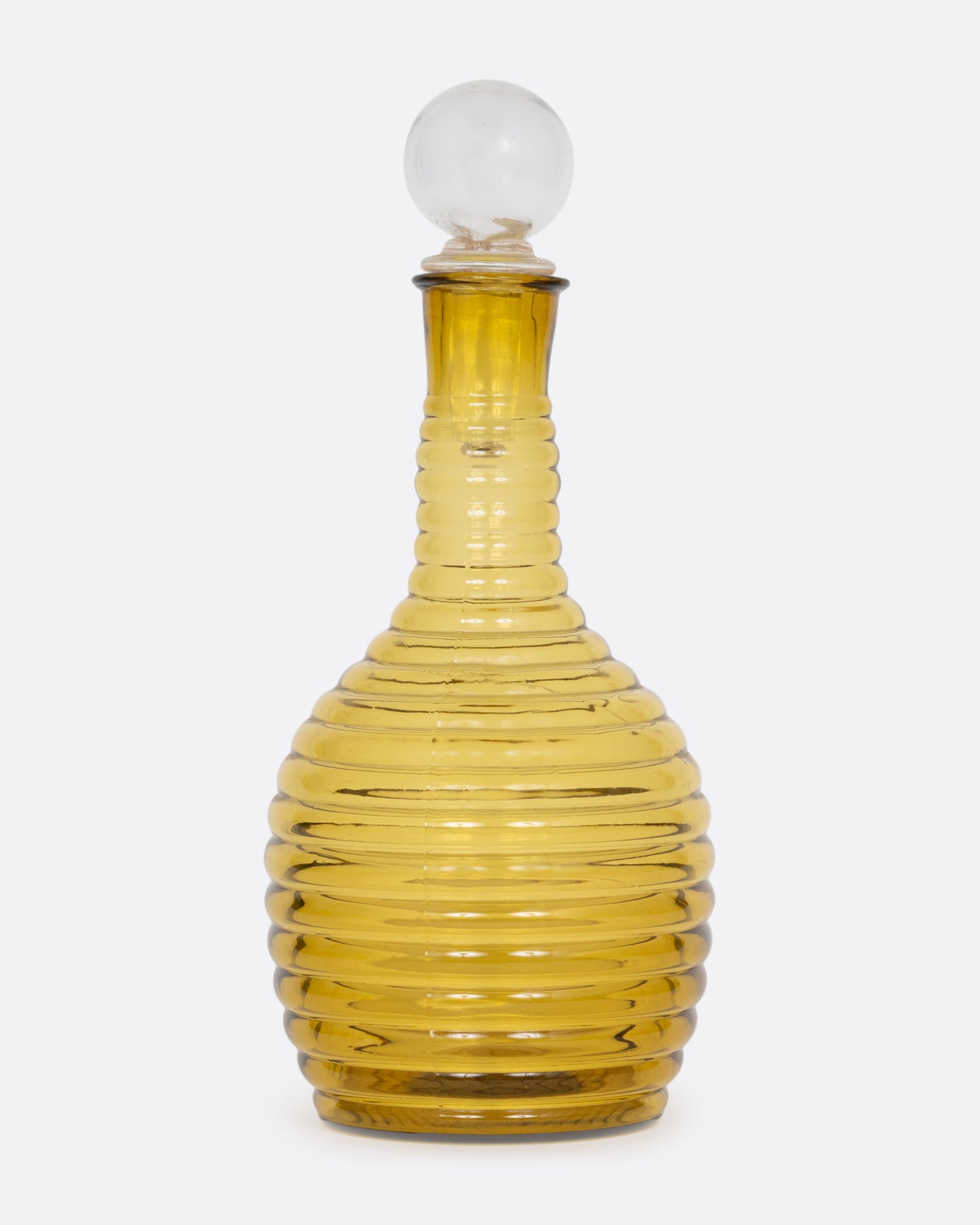 An amber colored beehive shaped glass decanter with a clear sphere shaped stopper. Shown from the front.