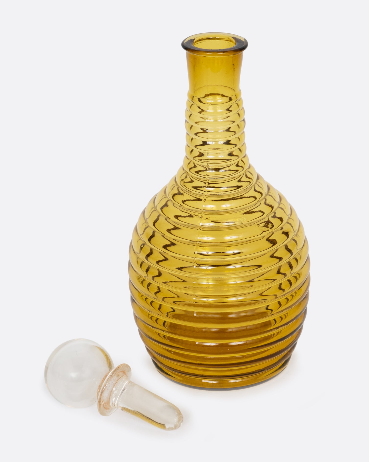 An amber colored beehive shaped glass decanter with a clear sphere shaped stopper. Shown open with the top lying flat from the side.