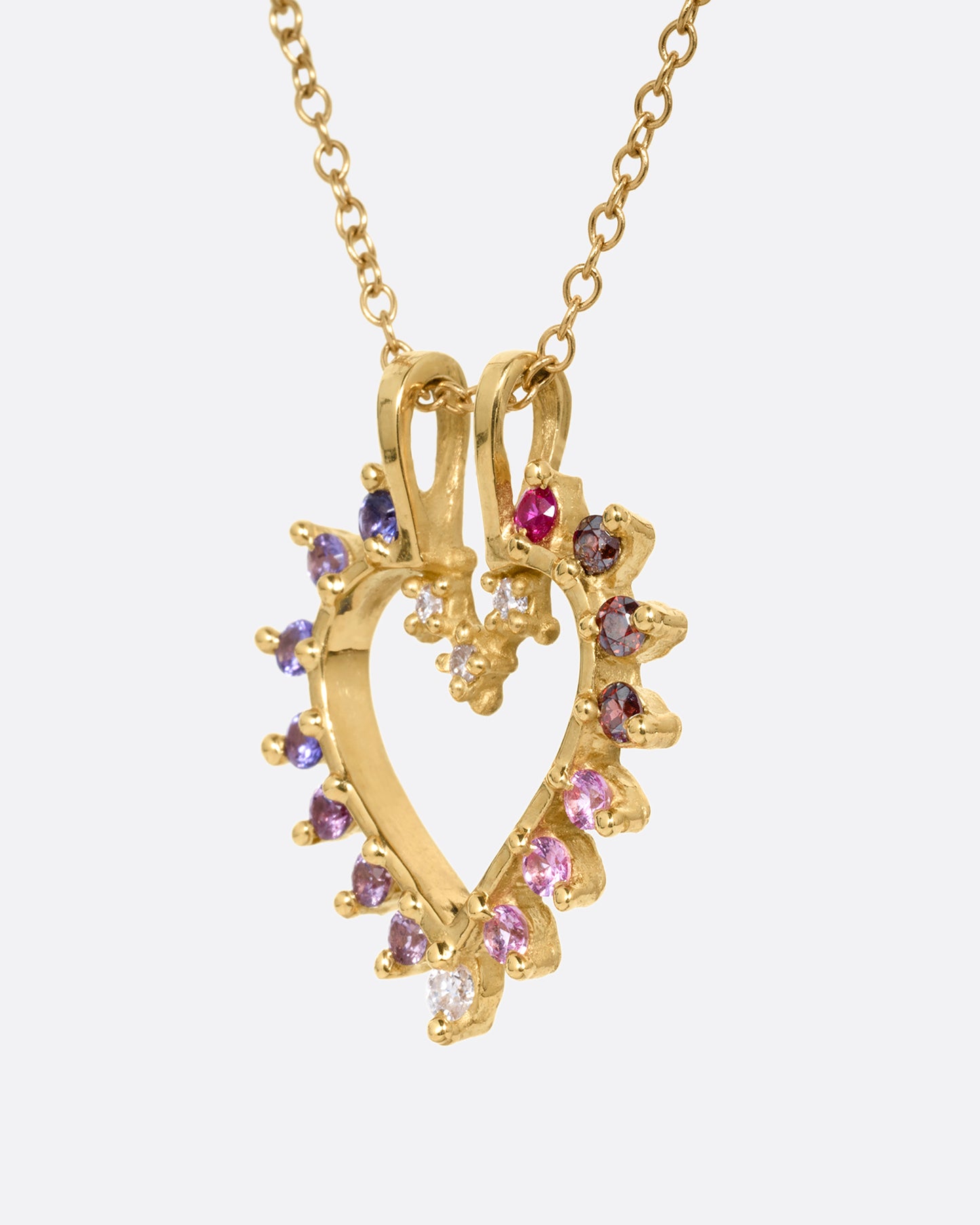 A yellow gold cable chain necklace with a heart shaped pendant with diamonds, rubies, and tourmalines. Shown from the side.