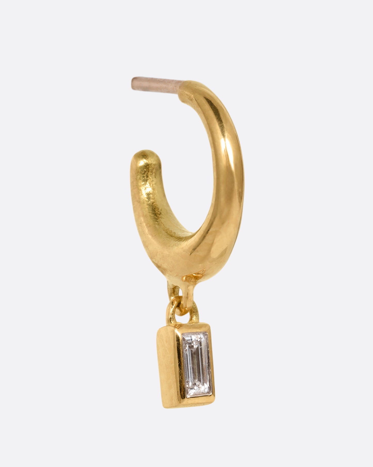 A yellow gold huggie hoop earring with a baguette diamond dangle. Shown from the side.