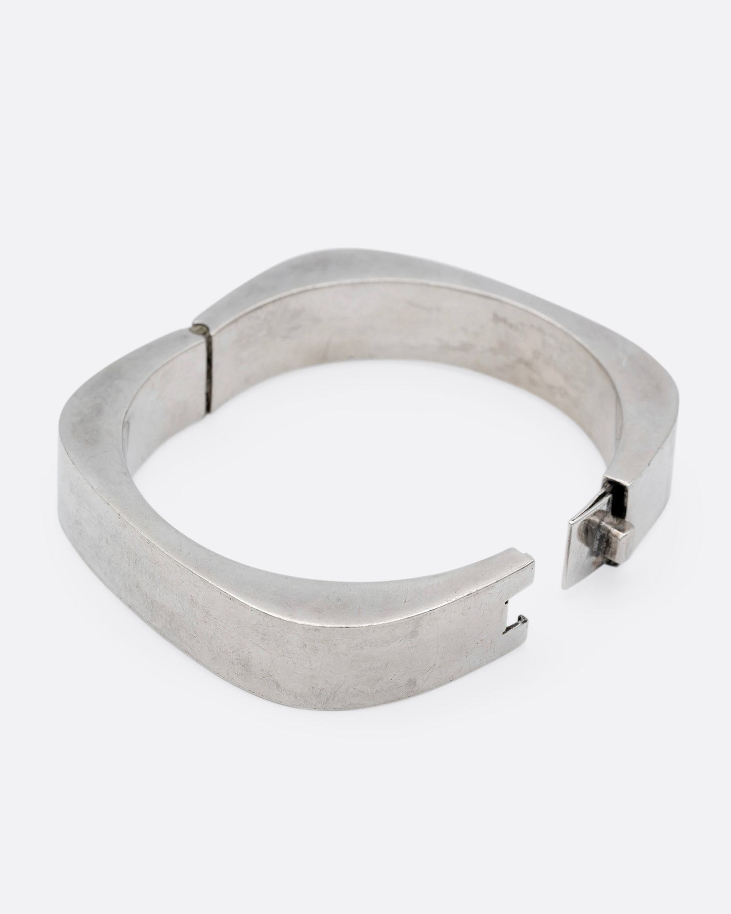 A thick square silver bracelet with a hinge and clasp. Shown open from the side.