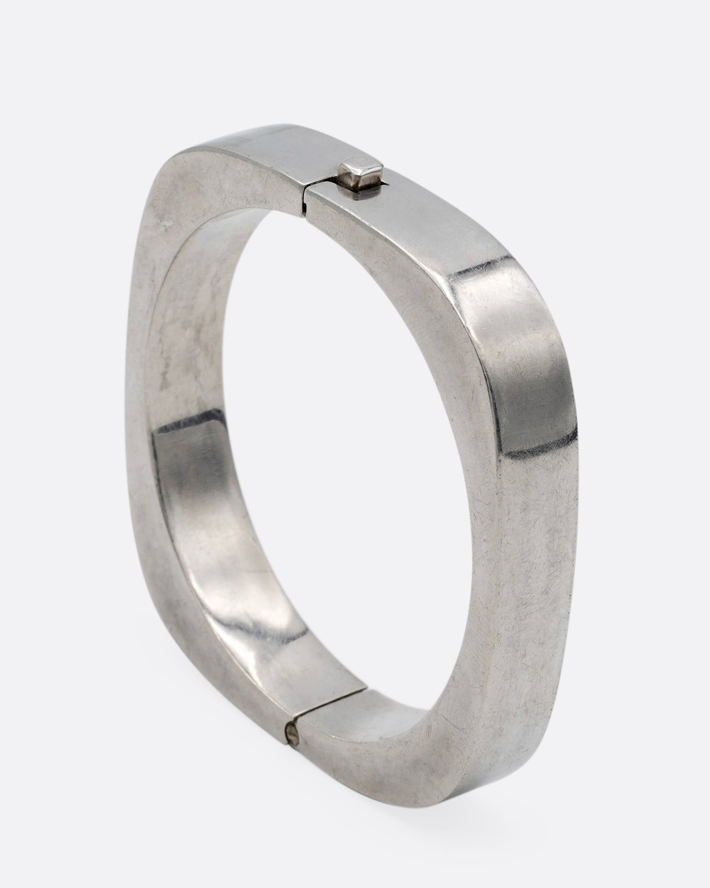 A thick square silver bracelet with a hinge and clasp. Shown standing up from the side.