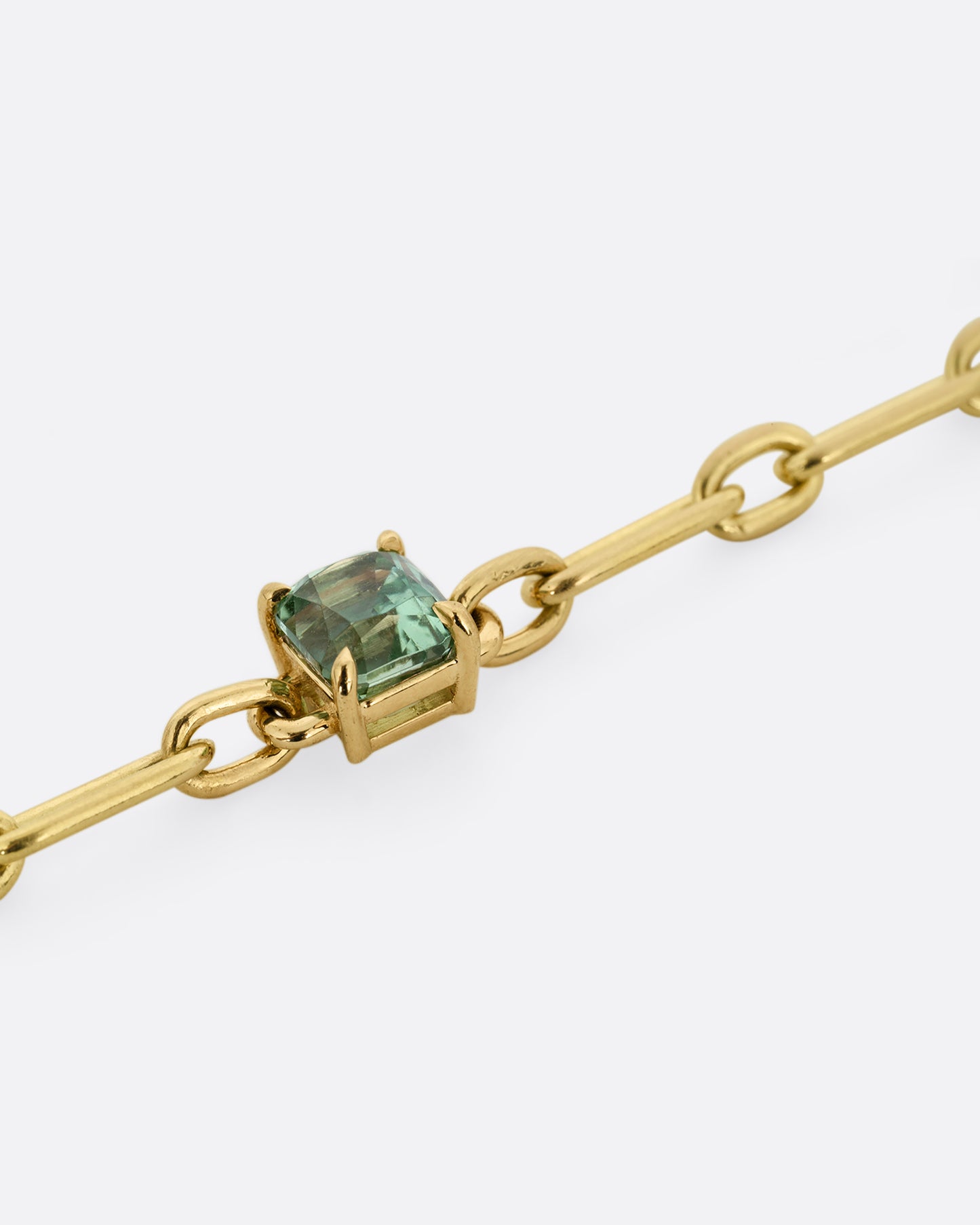 A close up of yellow gold chain link bracelet with a prong set aqua tourmaline at the center. Shown from the front.
