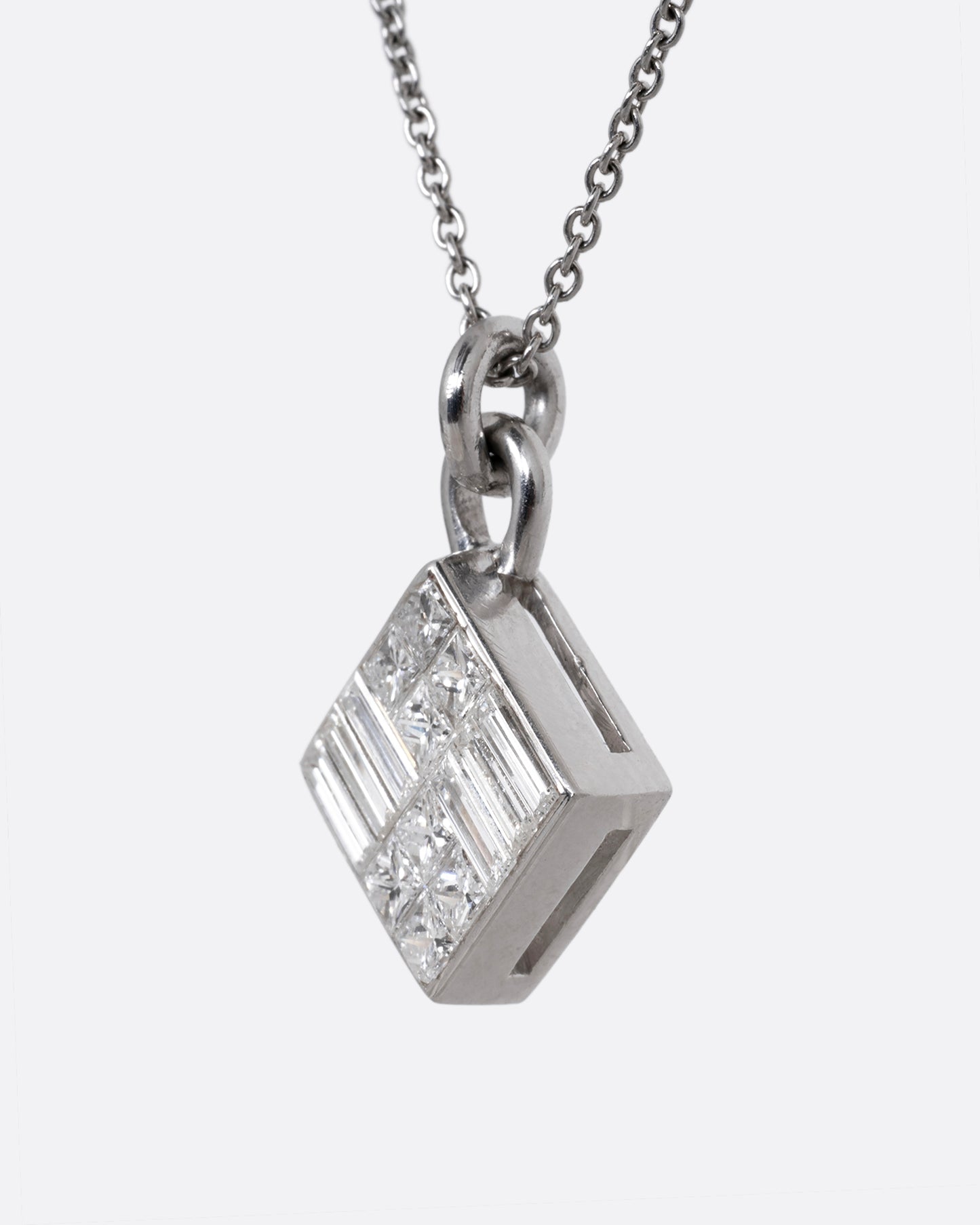 A white gold cable chain necklace with a pendant of princess cut and baguette diamonds. Shown from the side.