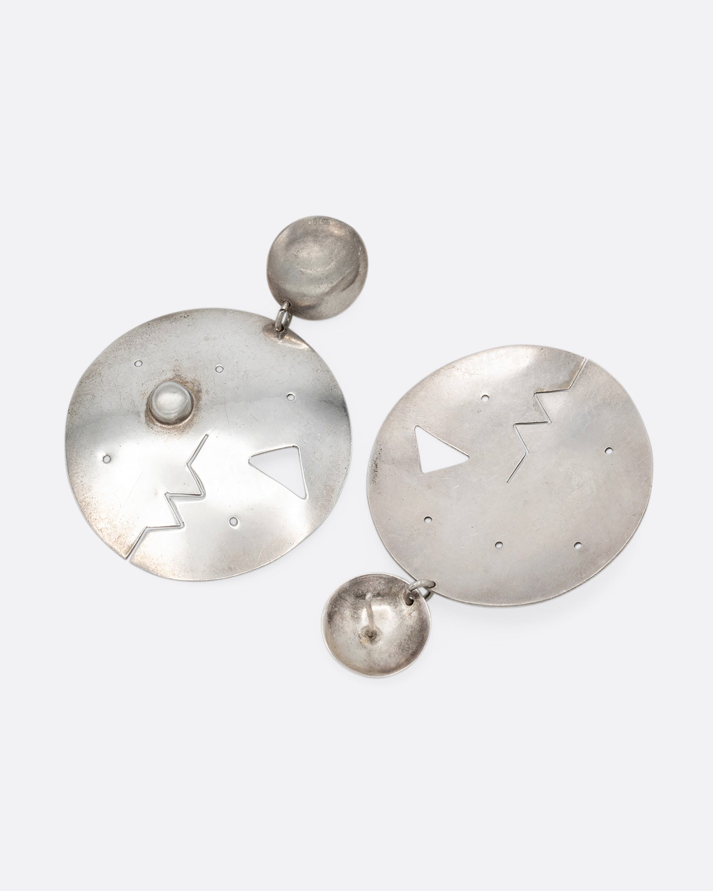 A pair of round drop stud earrings with geometric cutout faces. Shown lying flat.