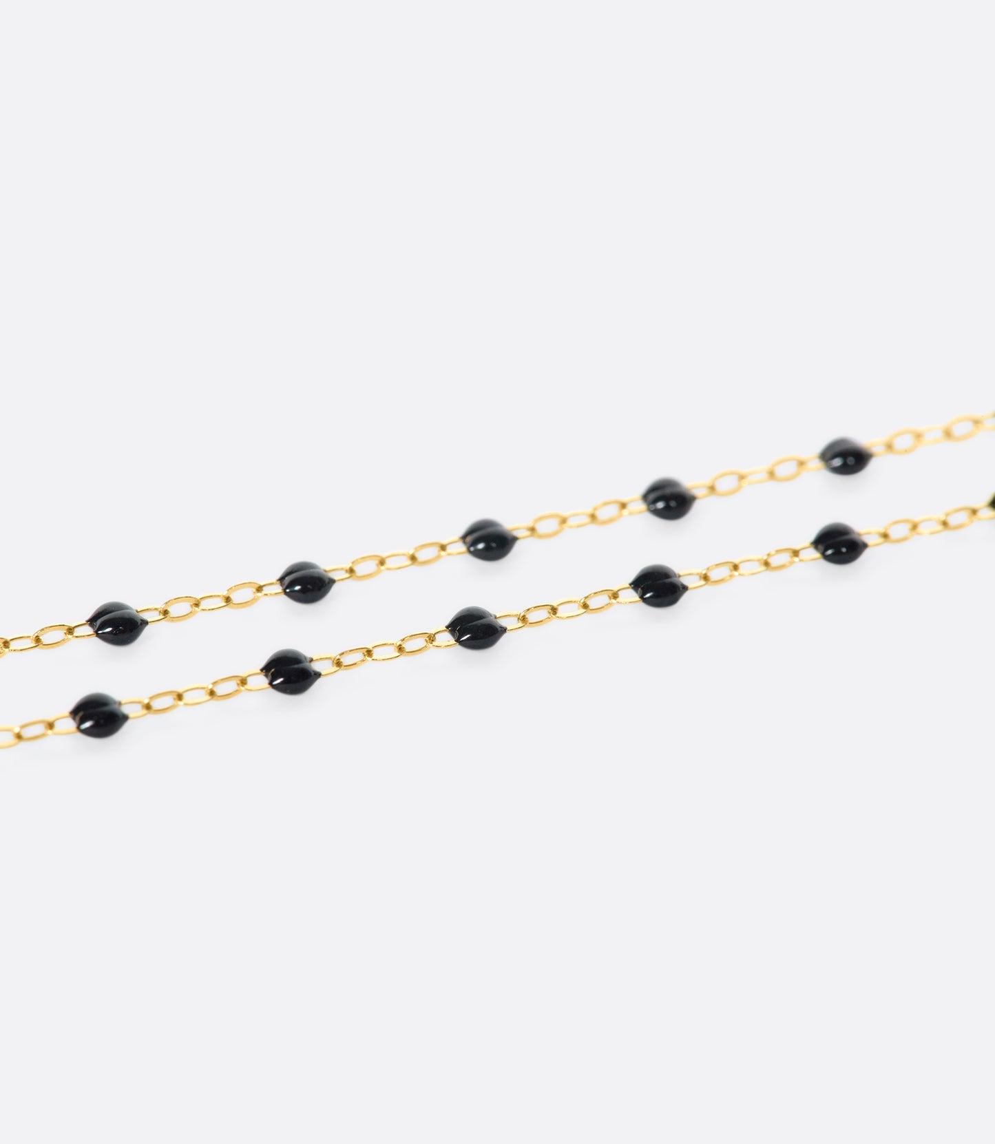 A close up view of a yellow gold cable chain necklace with black resin droplets. Shown from the side.