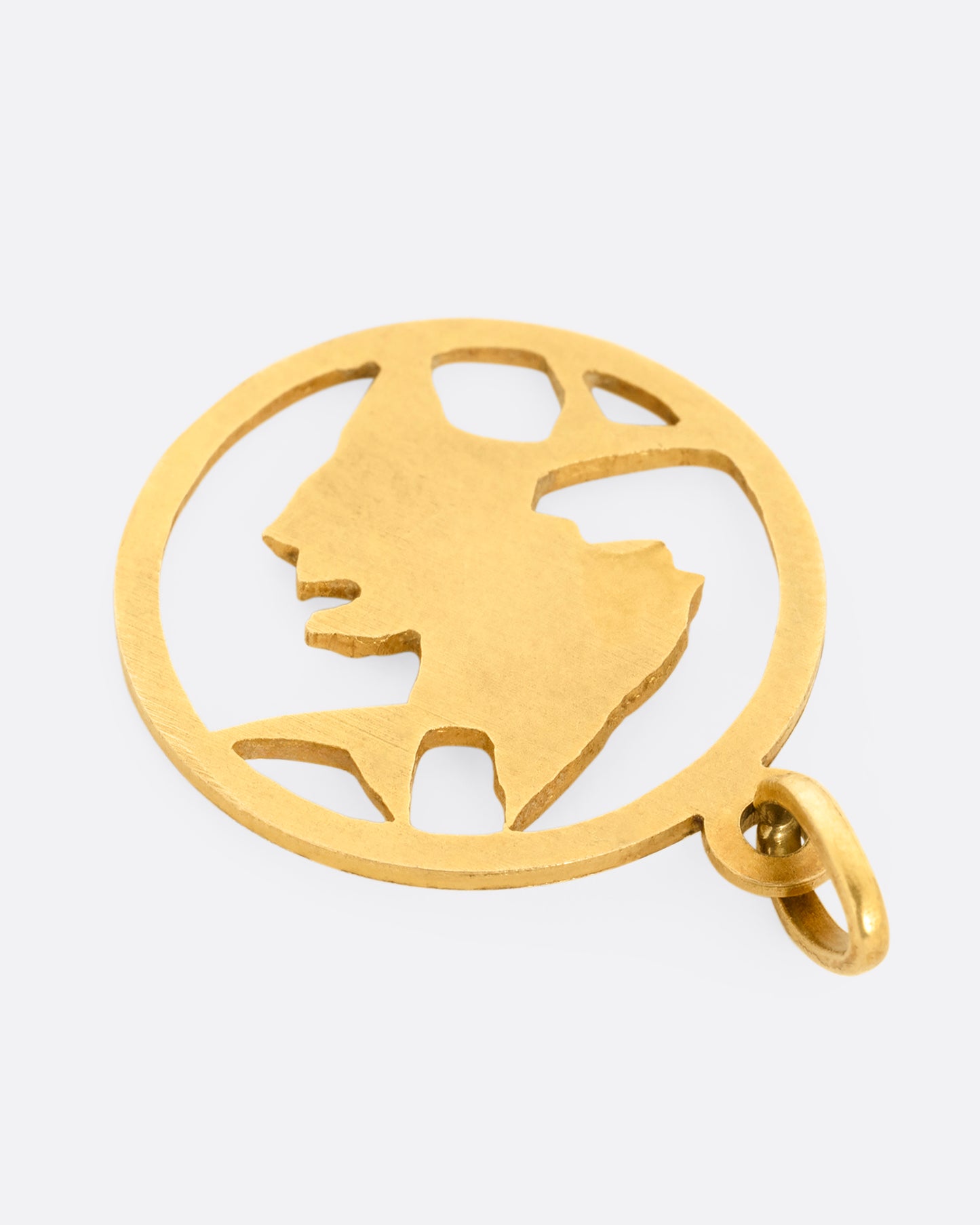 A circular yellow gold pendant with two fish and on open center with cutouts. Shown from the back.