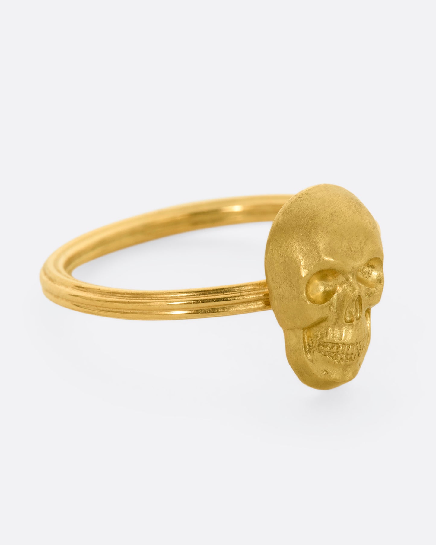 Side view of yellow gold ring with a sculpted skull charm on a round fluted band.