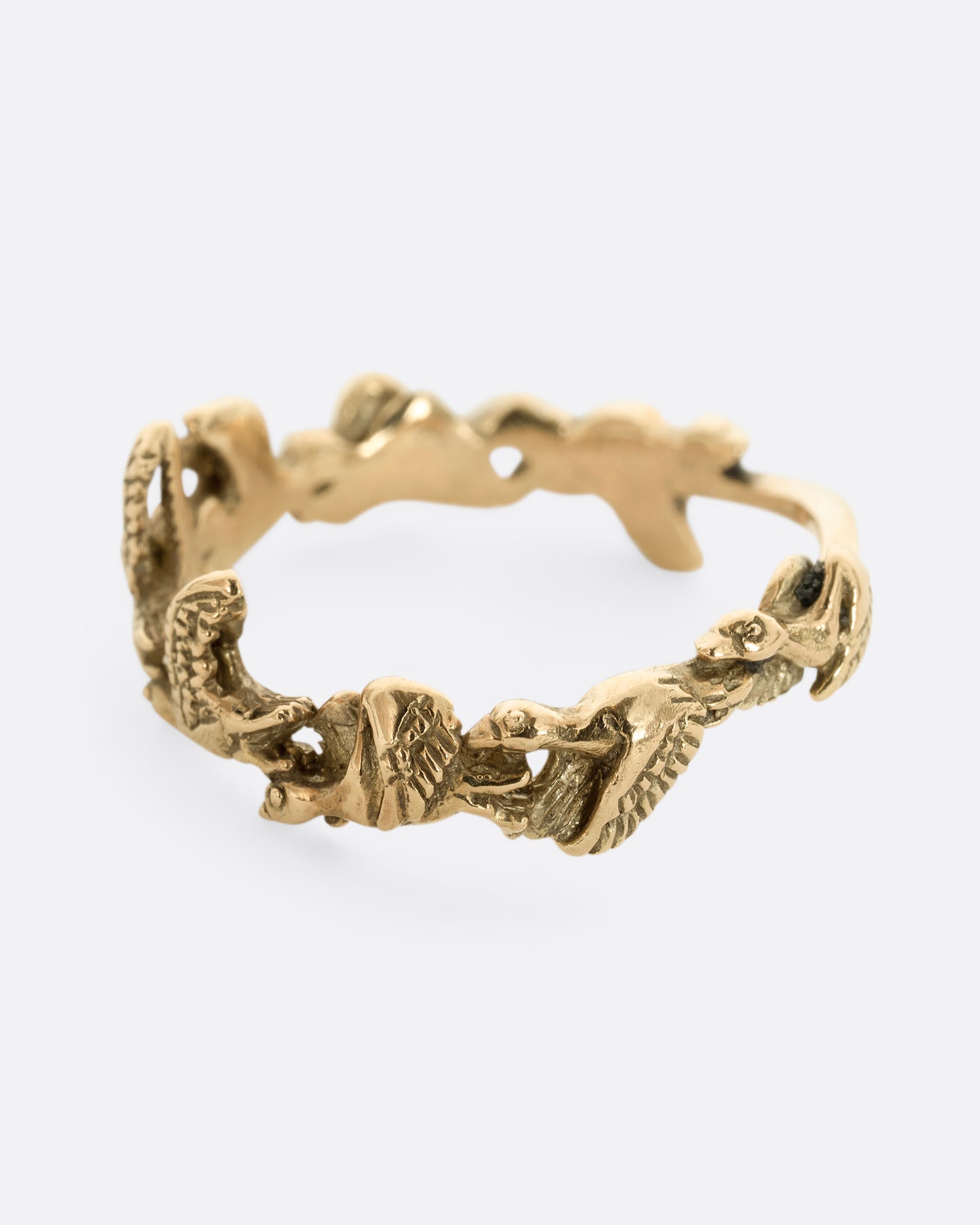 A yellow gold ring with birds flying around the majority of the band. Shown from the side.