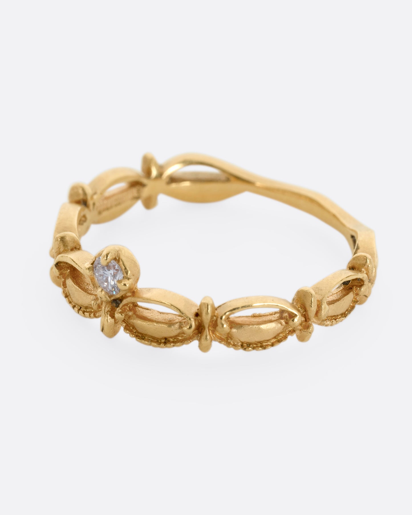 A yellow gold tiara shaped band with curved and textured details and a round white diamond at the center. Shown from the side.