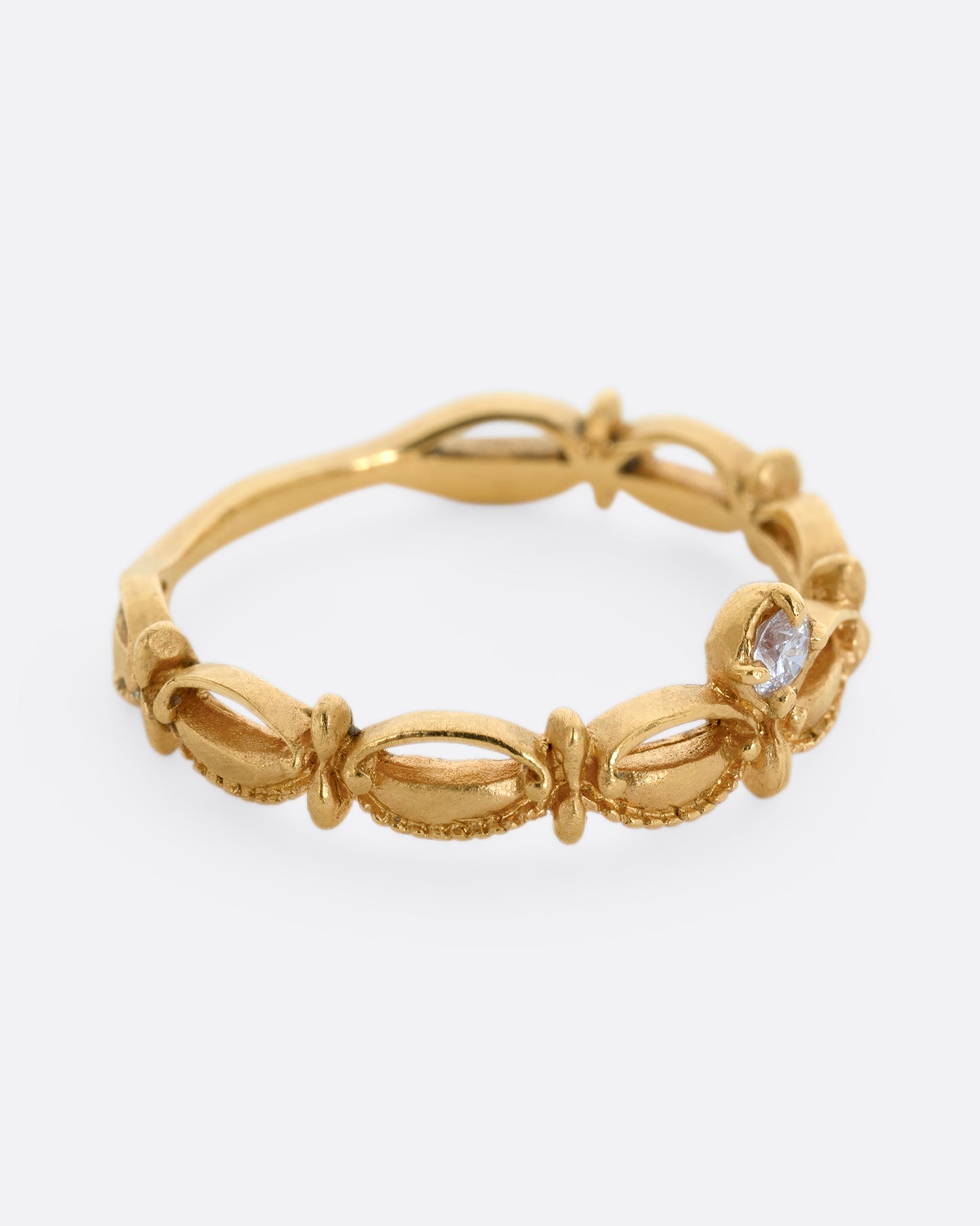 A yellow gold tiara shaped band with curved and textured details and a round white diamond at the center. Shown from the side.