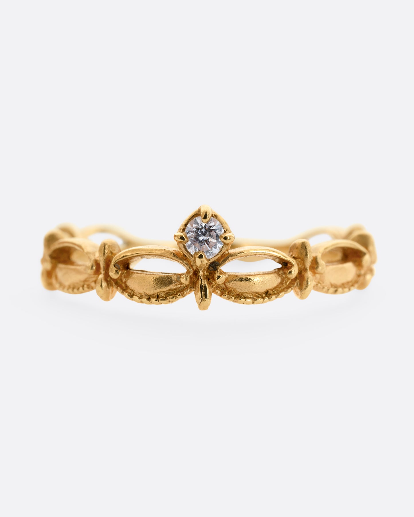 A yellow gold tiara shaped band with curved and textured details and a round white diamond at the center. Shown from the front.