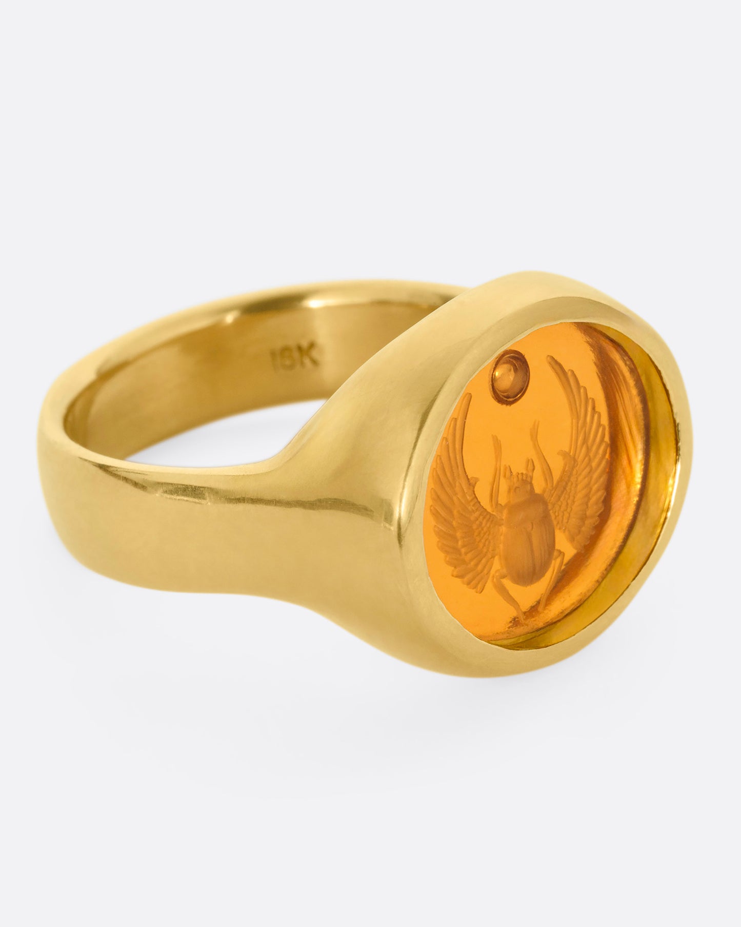 A yellow gold signet ring with a citrine with a hand carved scarab, shown from the side.