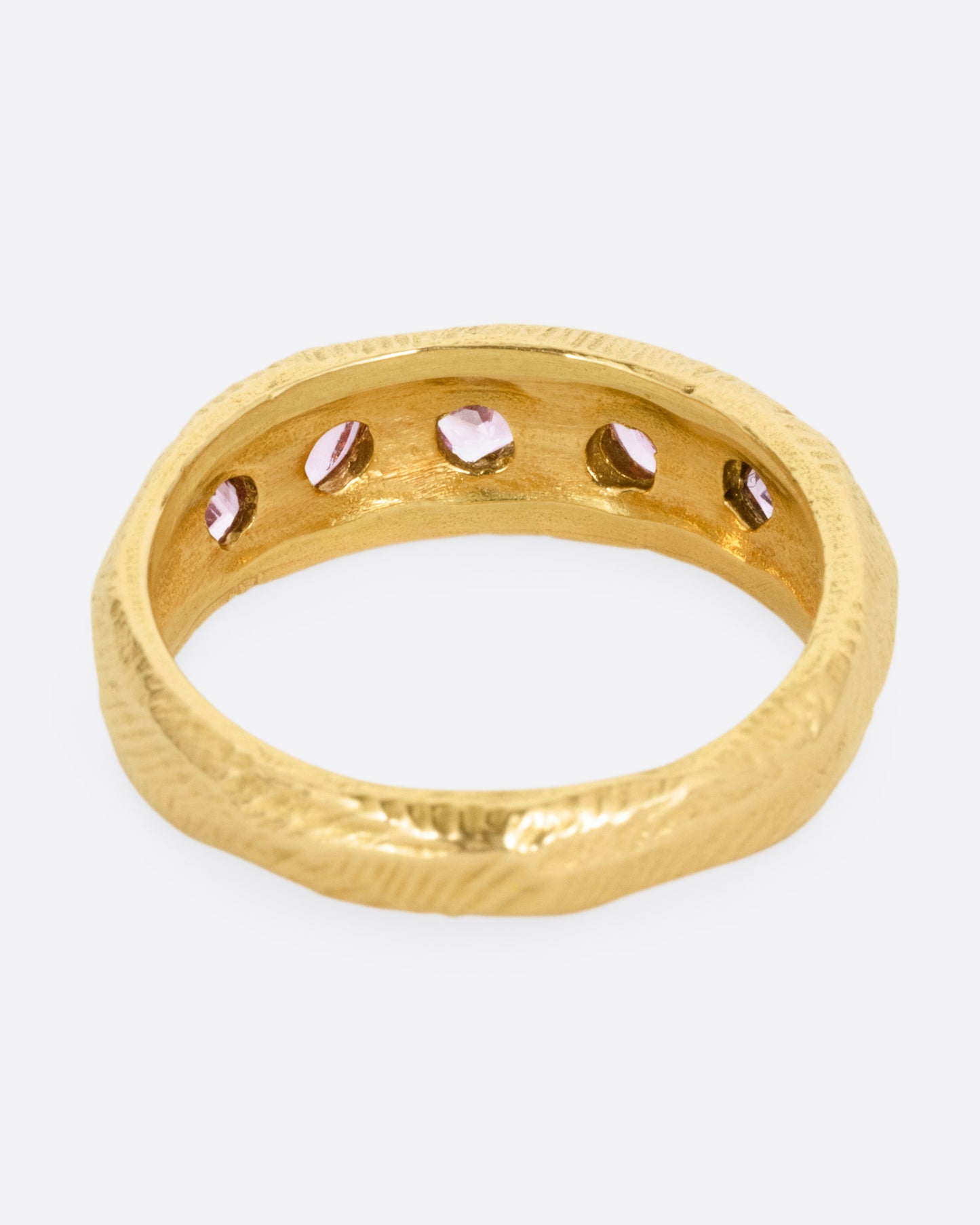 A yellow gold band with five pink sapphires, shown from the back.
