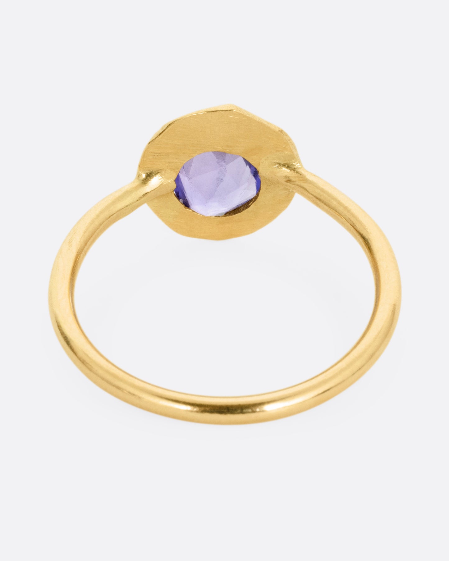 A yellow gold ring with a purple blue sapphire, shown from the back.