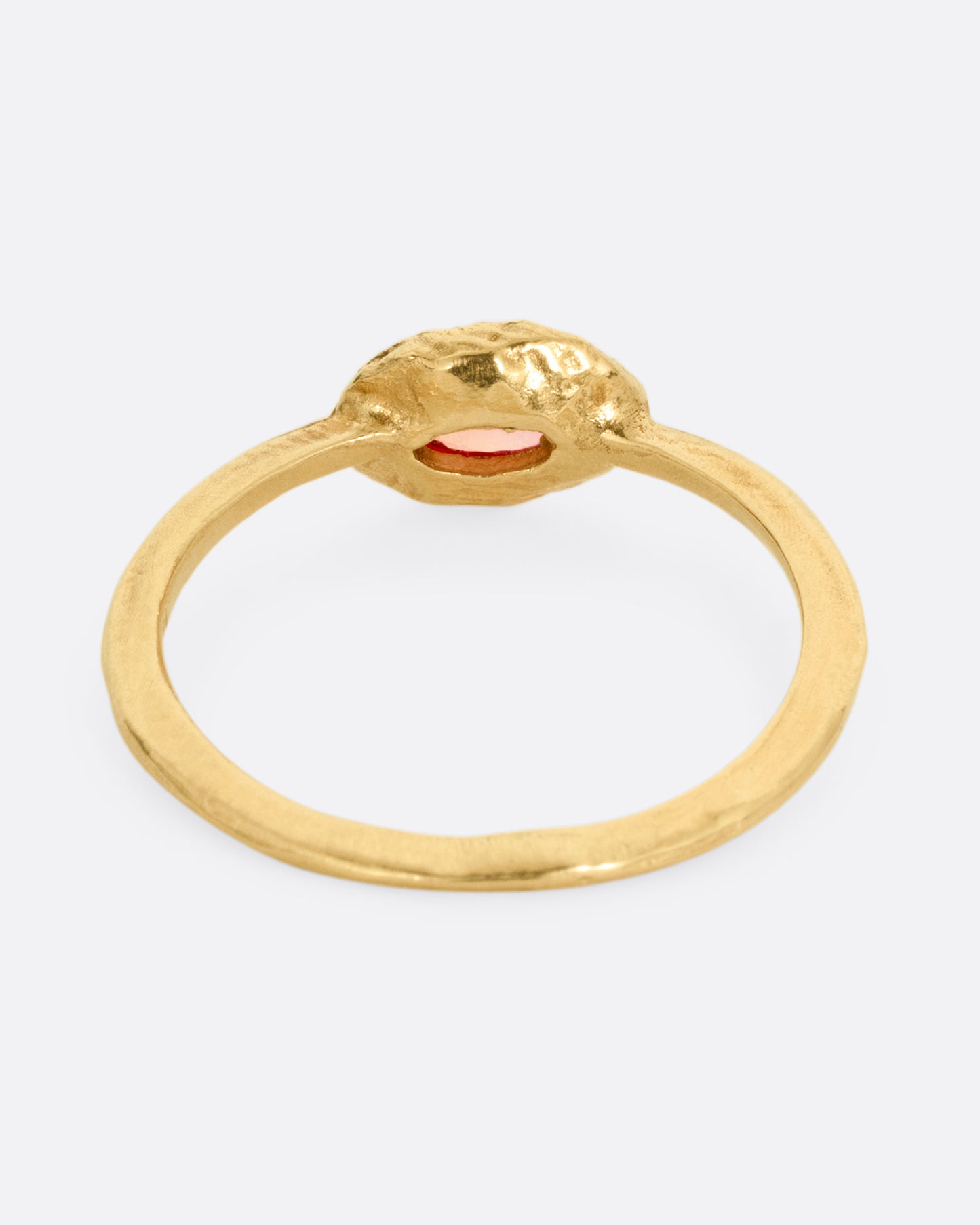 A yellow gold ring with a poppy red sapphire bezel set in a hand carved band. Shown from the back.