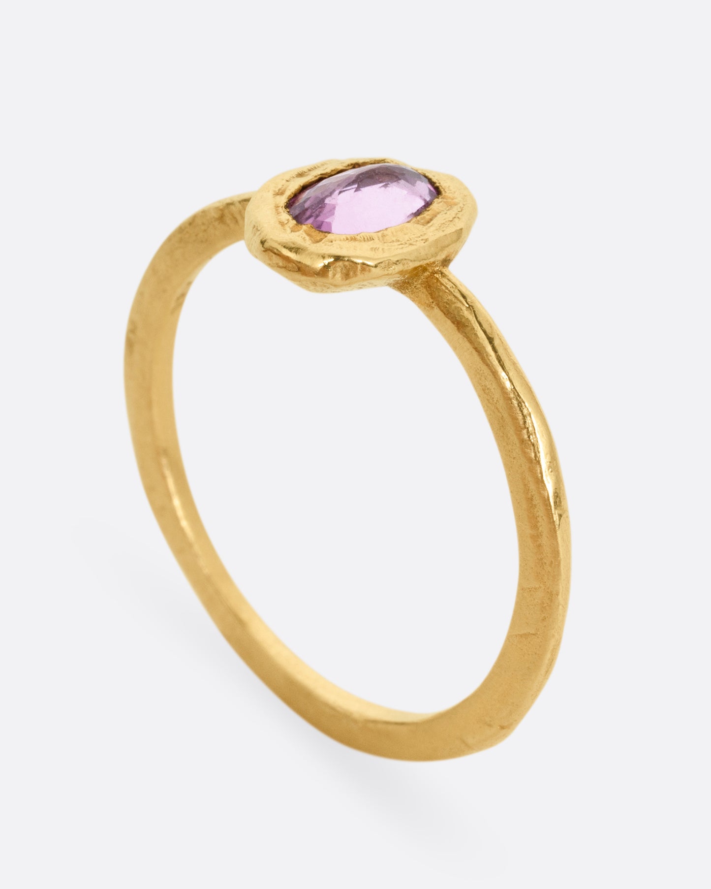 A yellow gold ring with a pale pink sapphire in a hand carved bezel. Shown from the side standing up.