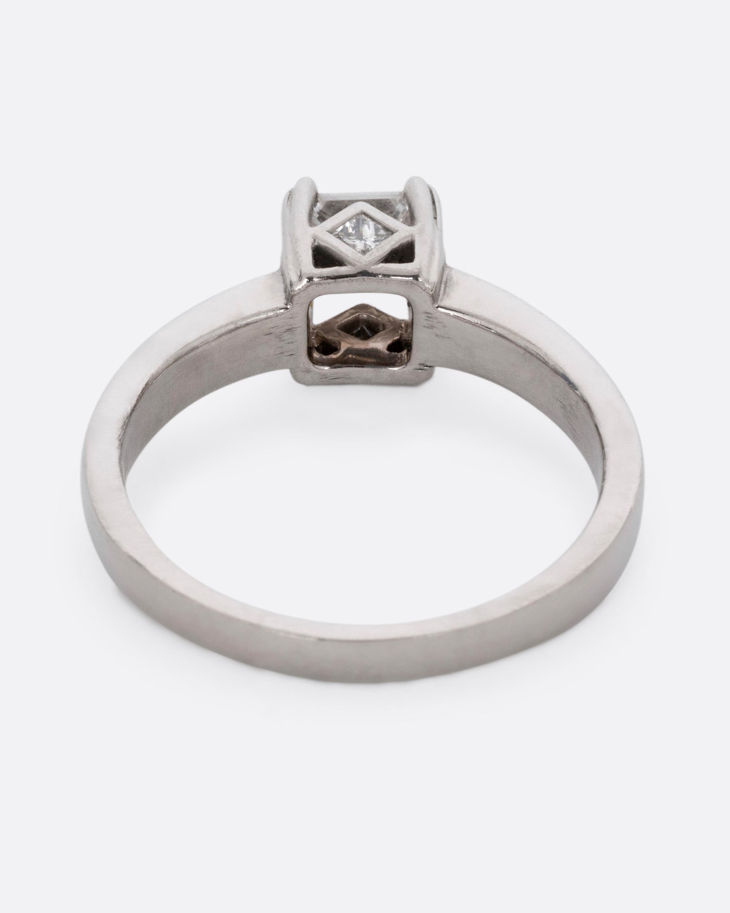 A platinum ring with a princess cut diamond, prong set high above angular cutouts and diamond accents. Shown from the back.