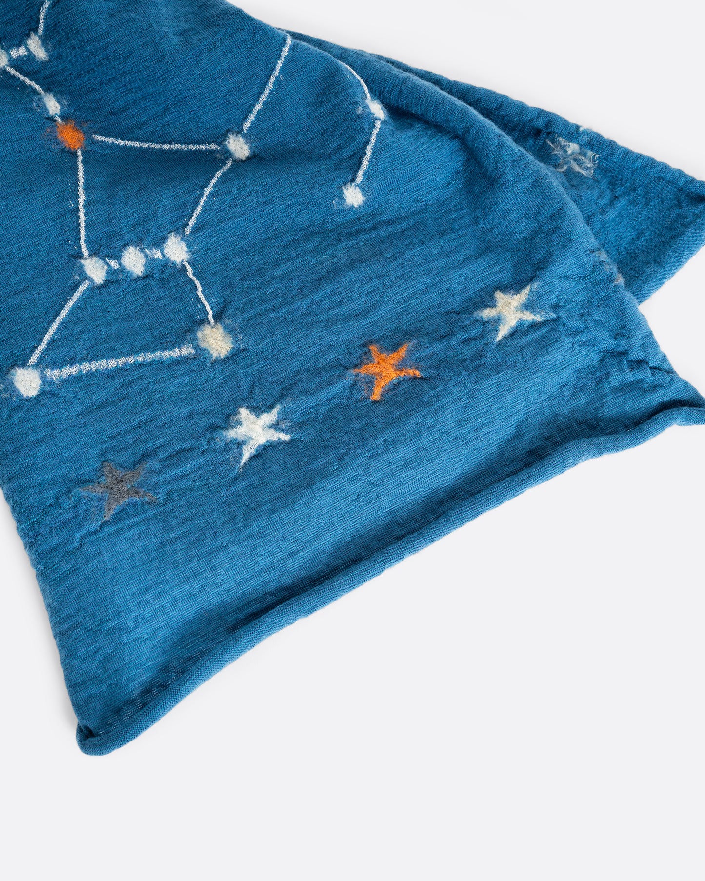 A light blue scarf with constellations novelty knit. Close up of the rolled hem.