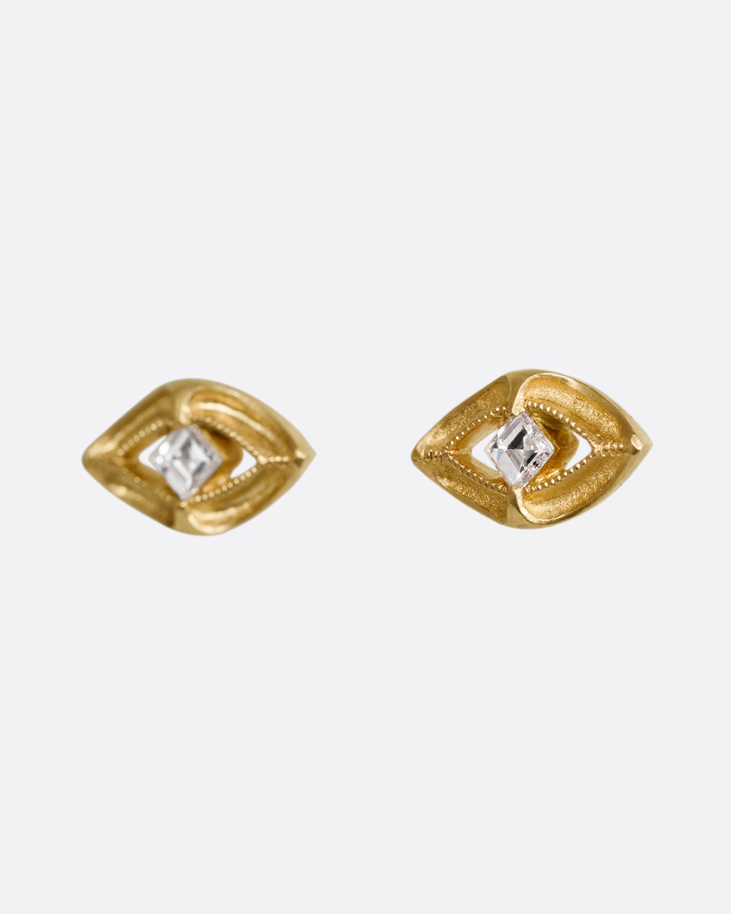 A pair of yellow gold earrings shaped like an eye with a diamond at the center. Shown from the side.
